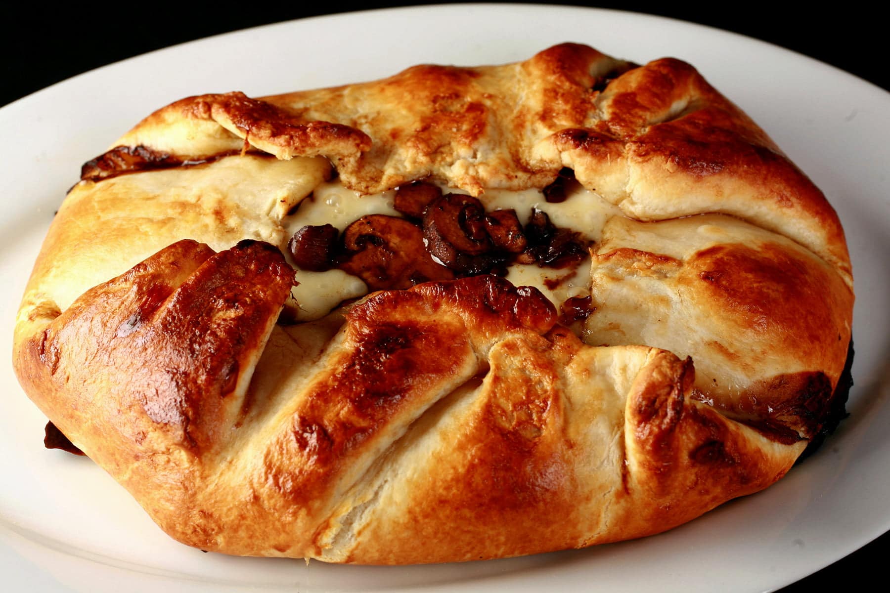 An oval shaped baked brie. Melted cheese and mushrooms are visible in the center.