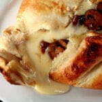 A balsamic mushroom baked brie is broken open, with melted cheese and sauteed mushrooms oozing out onto a white plate.