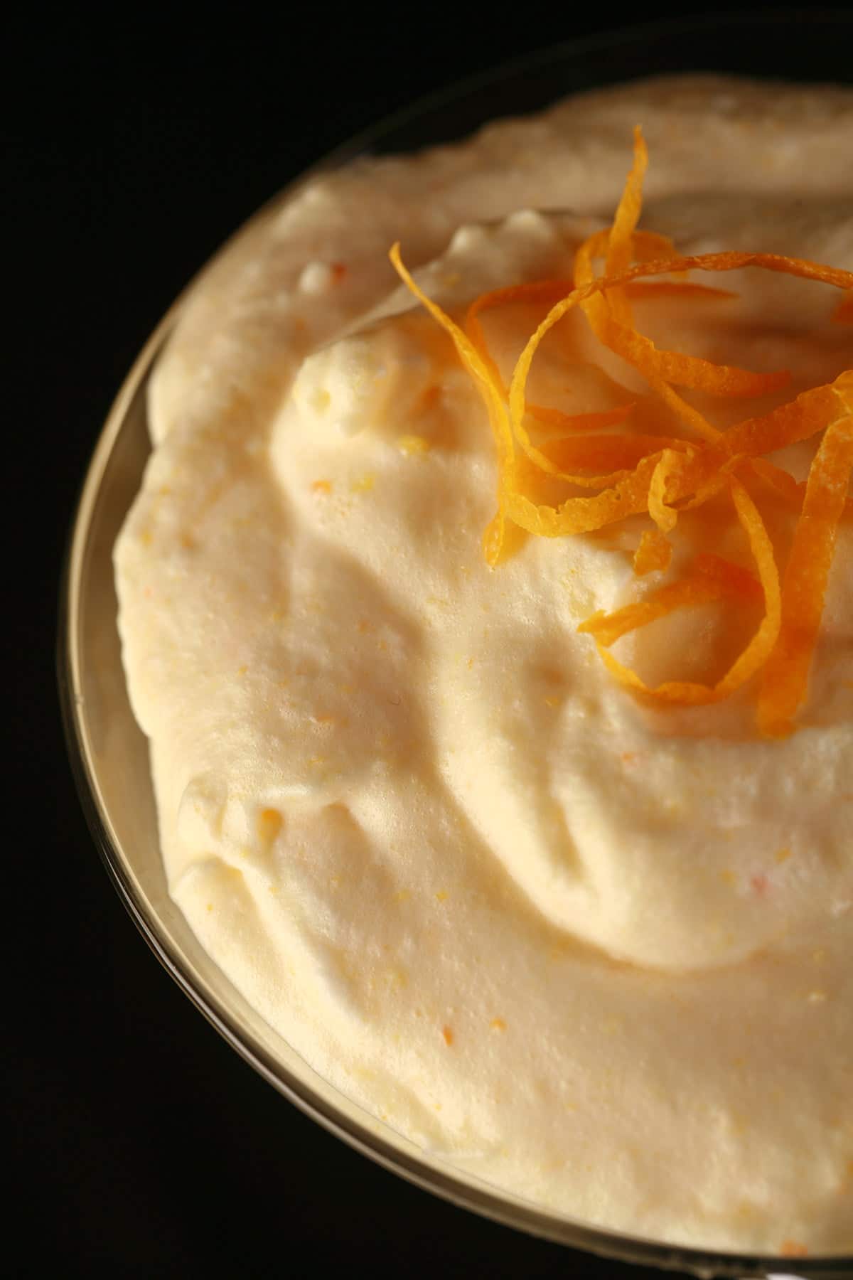 A very close up view of lightly orange coloured mousse. It has a small mound of clementine zest twists piled in the middle.