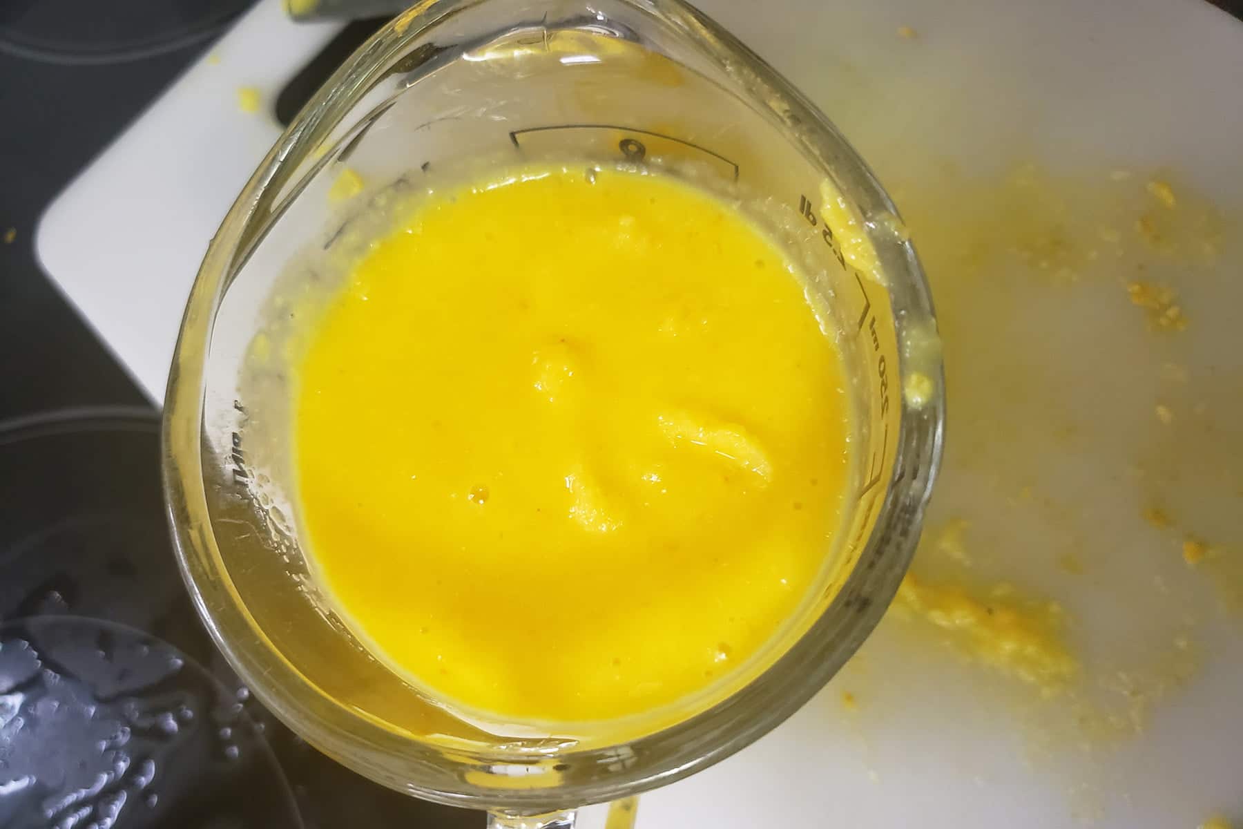 A glass measuring cup contains bright yellow-orange fruit pulp.