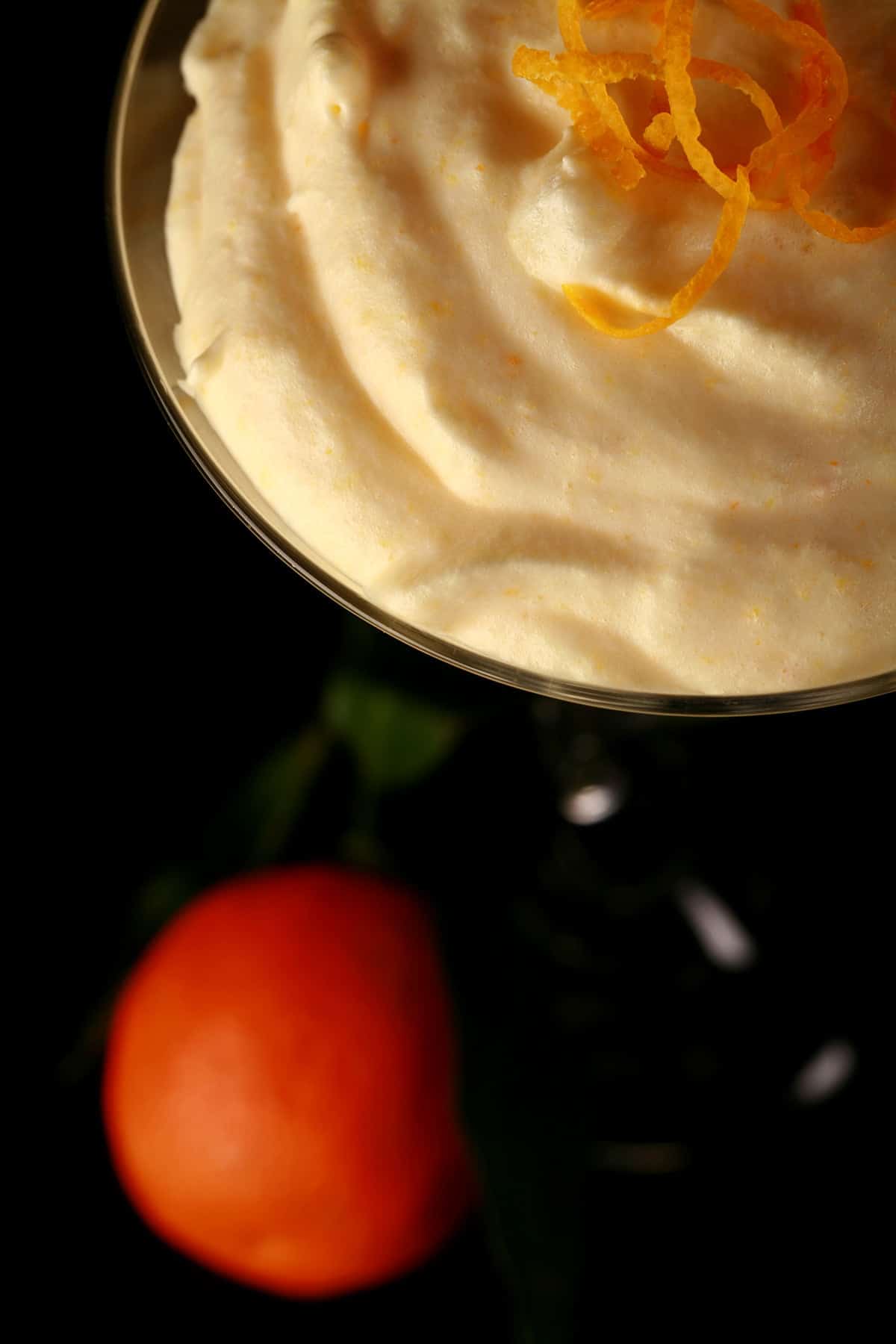 A martini glass is filled with an orange coloured clementine mousse. A clementine orange sits at the base of the glass.
