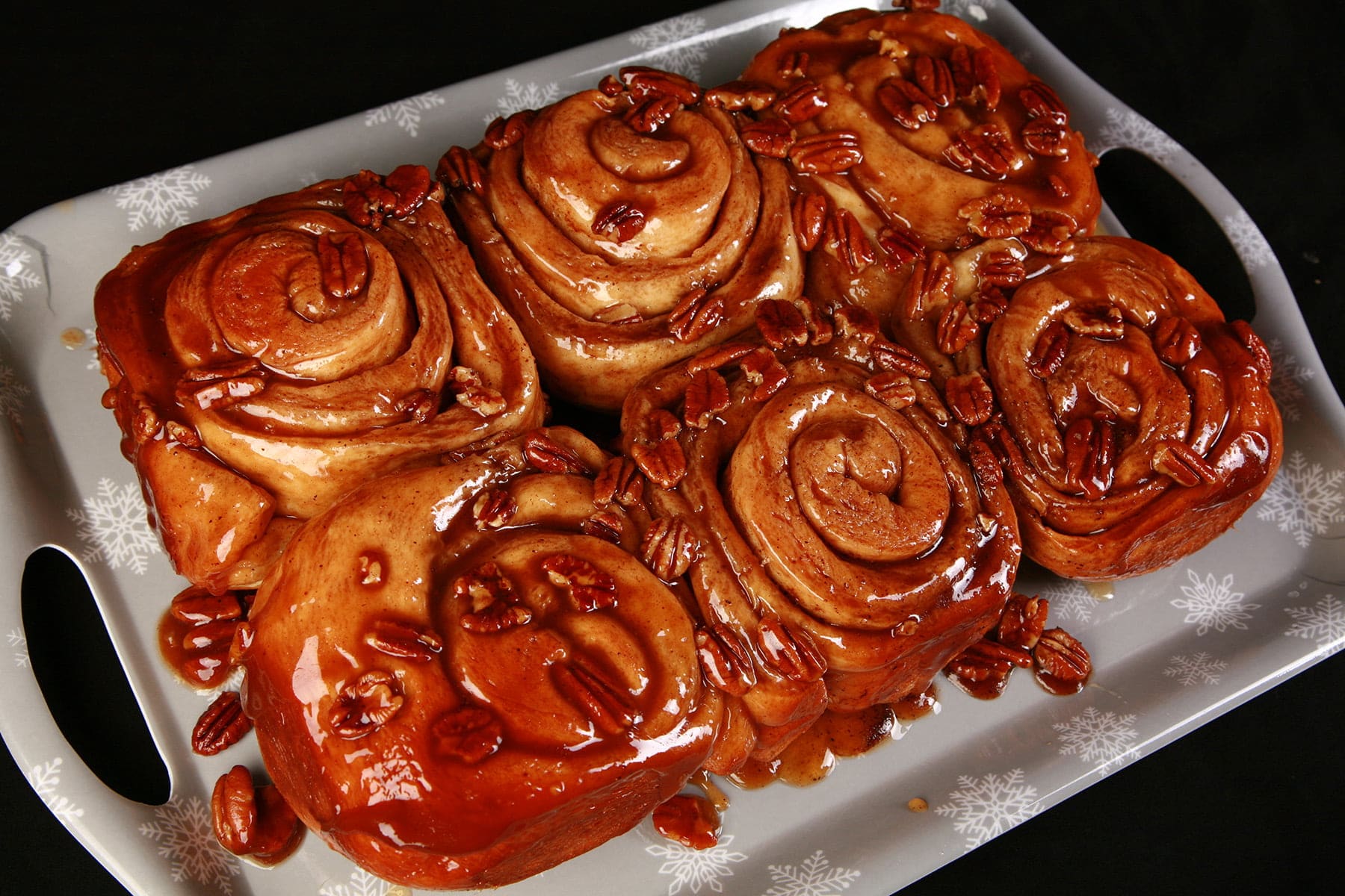 A close up view of a slab of 6 eggnog sticky buns. They are dripping with caramel and pecans.