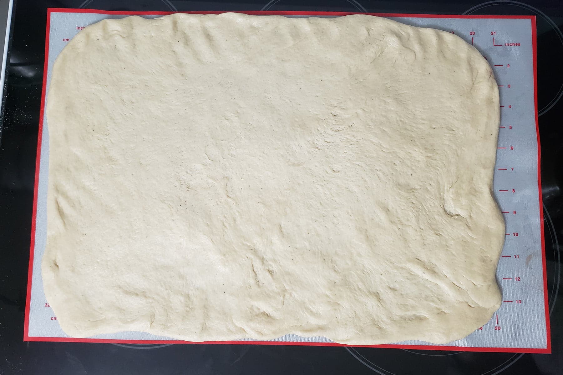 A large rectangle of dough is rolled out on a silicone baking sheet.
