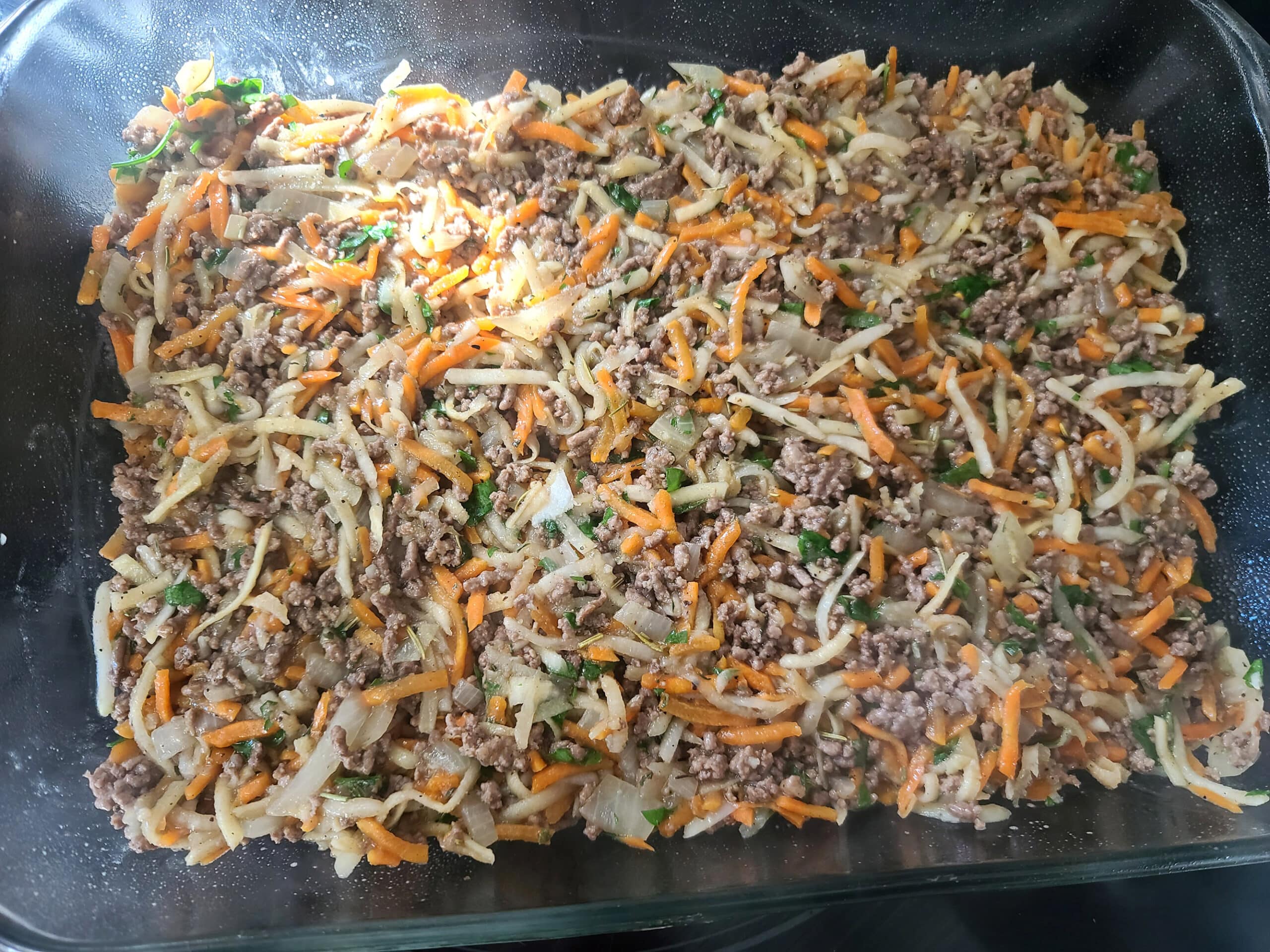 The ground beef and vegetable mixture being spread in a 8 x 13 inch pan.