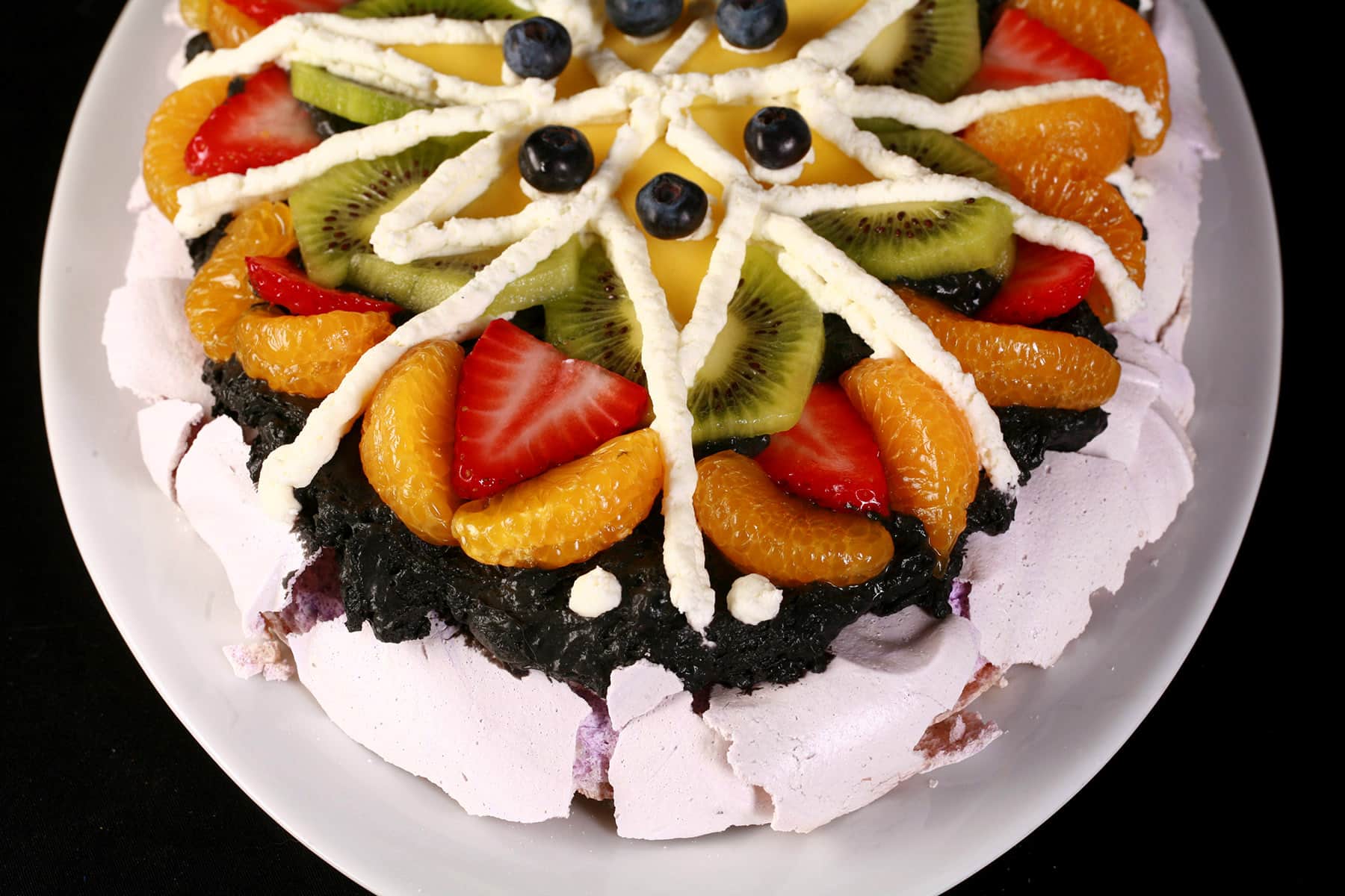 An oval shaped Easter pavlova decorated with fruit to look like a pysanky egg.