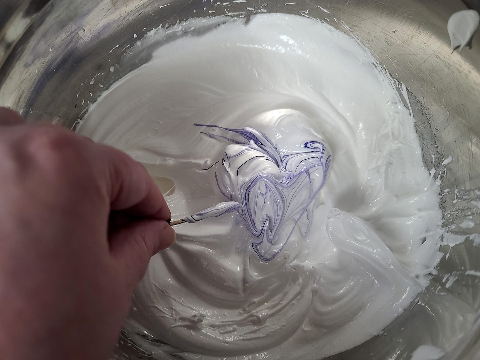 Purple food colouring being swirled into the whipped egg whites.