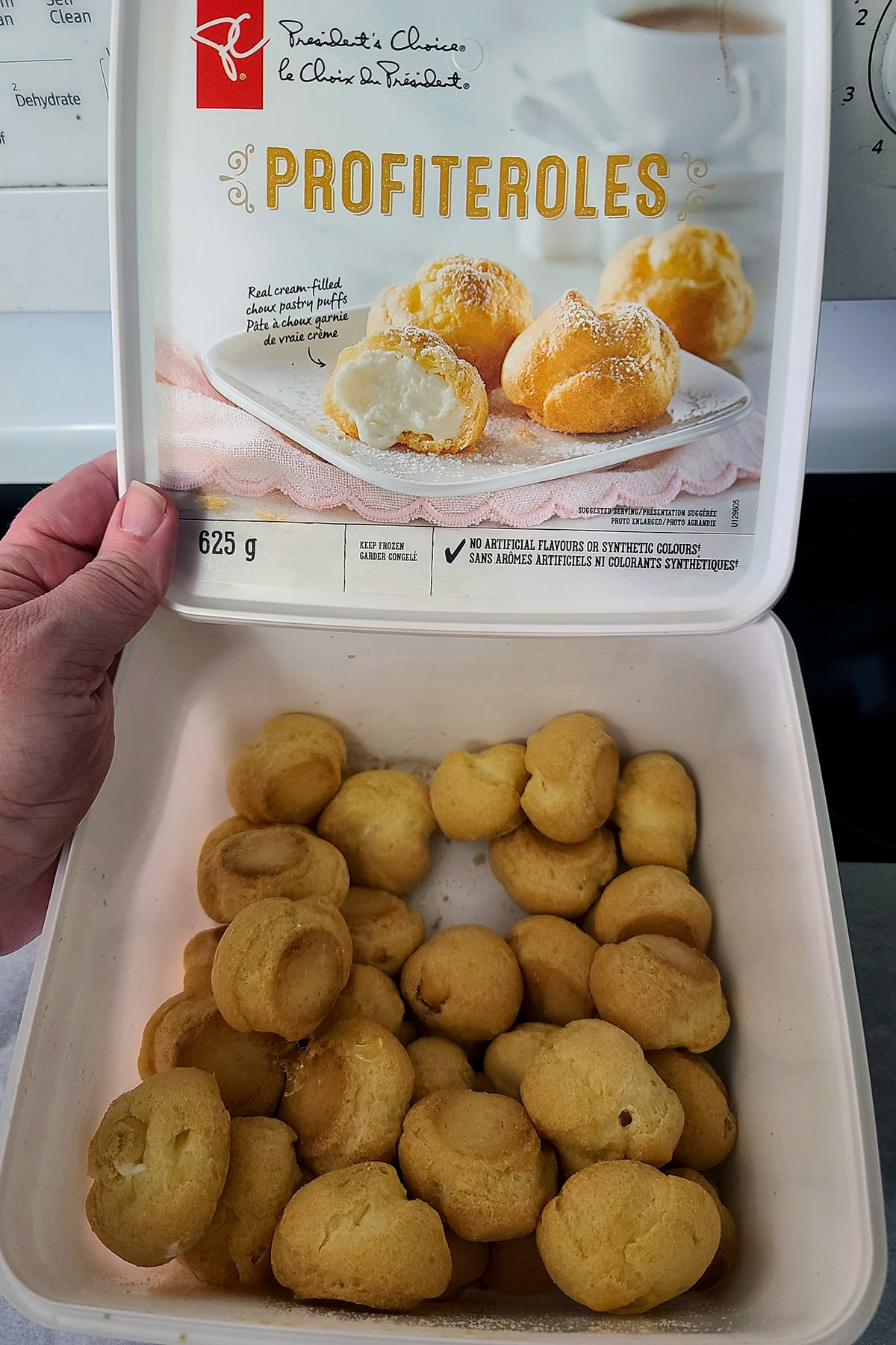 A hand holds open a box of frozen President’s Choice profiteroles.