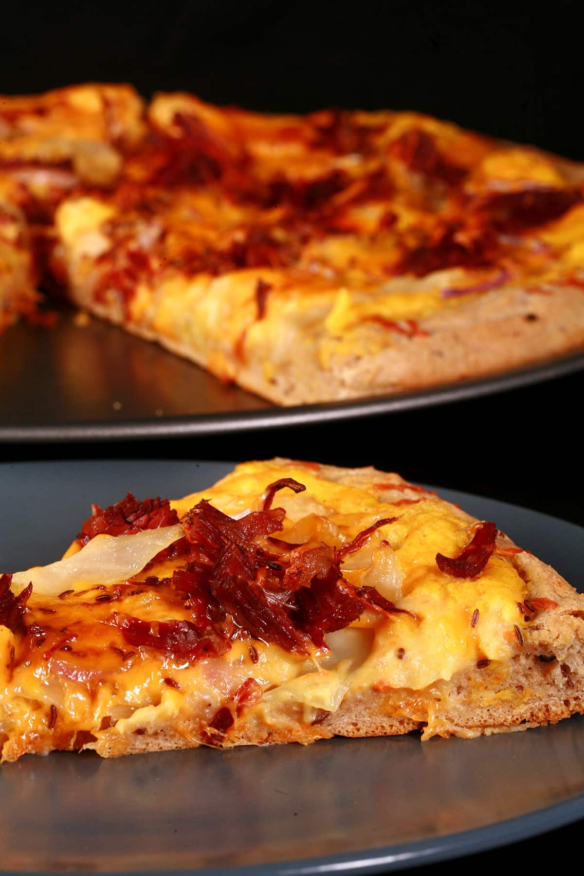 A slice of St Patrick’s Day Pizza on a plate in front of the rest of the pizza.