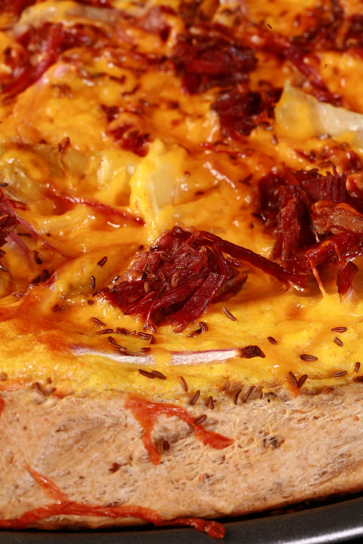 An overhead view of an Irish Pizza - a large rye crust pizza with cabbage, corned beef, cheddar, caraway seeds, and more.