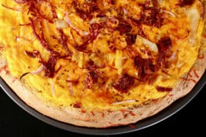 An overhead view of an Irish Pizza - a large rye crust pizza with cabbage, corned beef, cheddar, caraway seeds, and more.