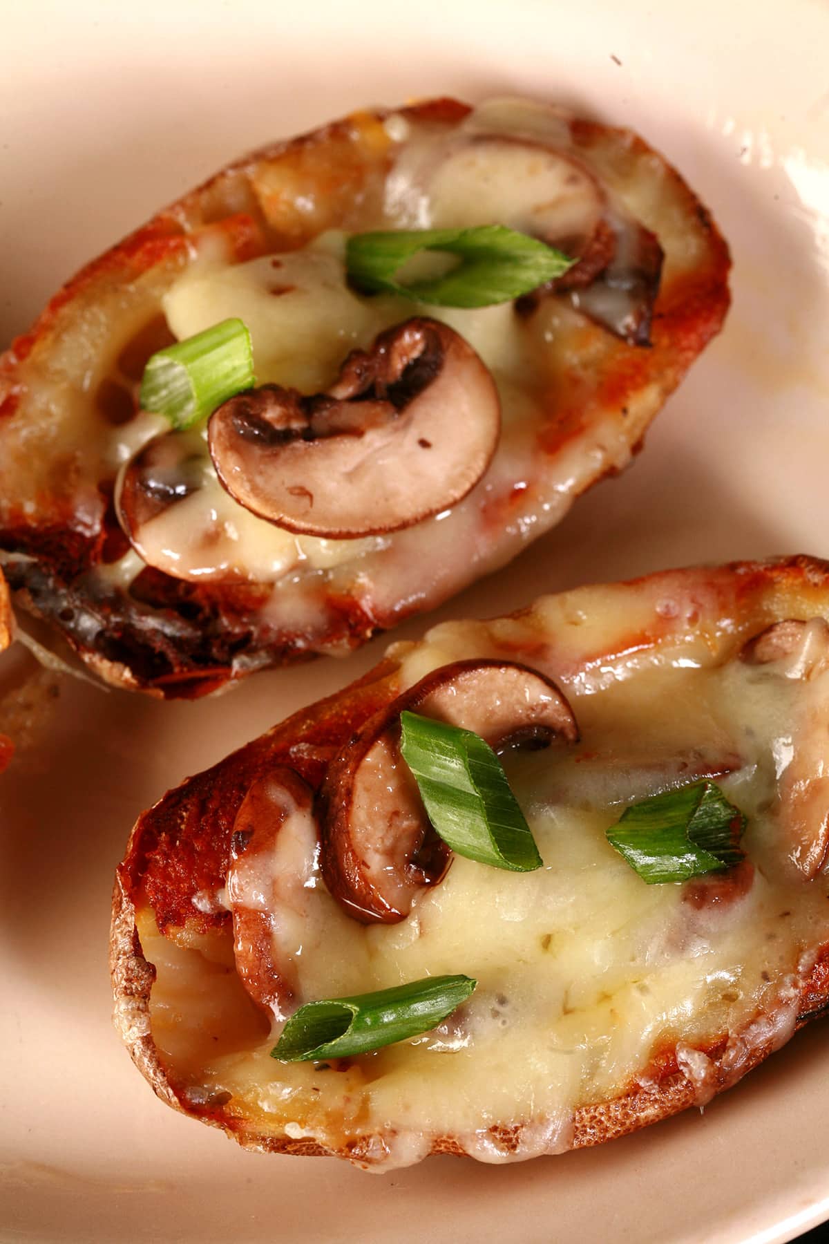 2 loaded potato skins on a plate - they’re topped with mushrooms, swiss cheese, and green onions.