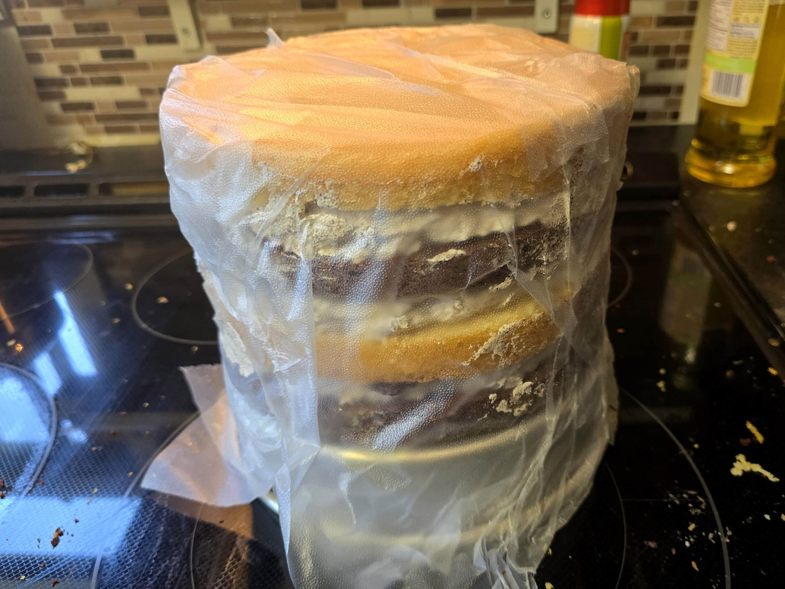 The layered cookies cake being wrapped in plastic wrap before chilling.