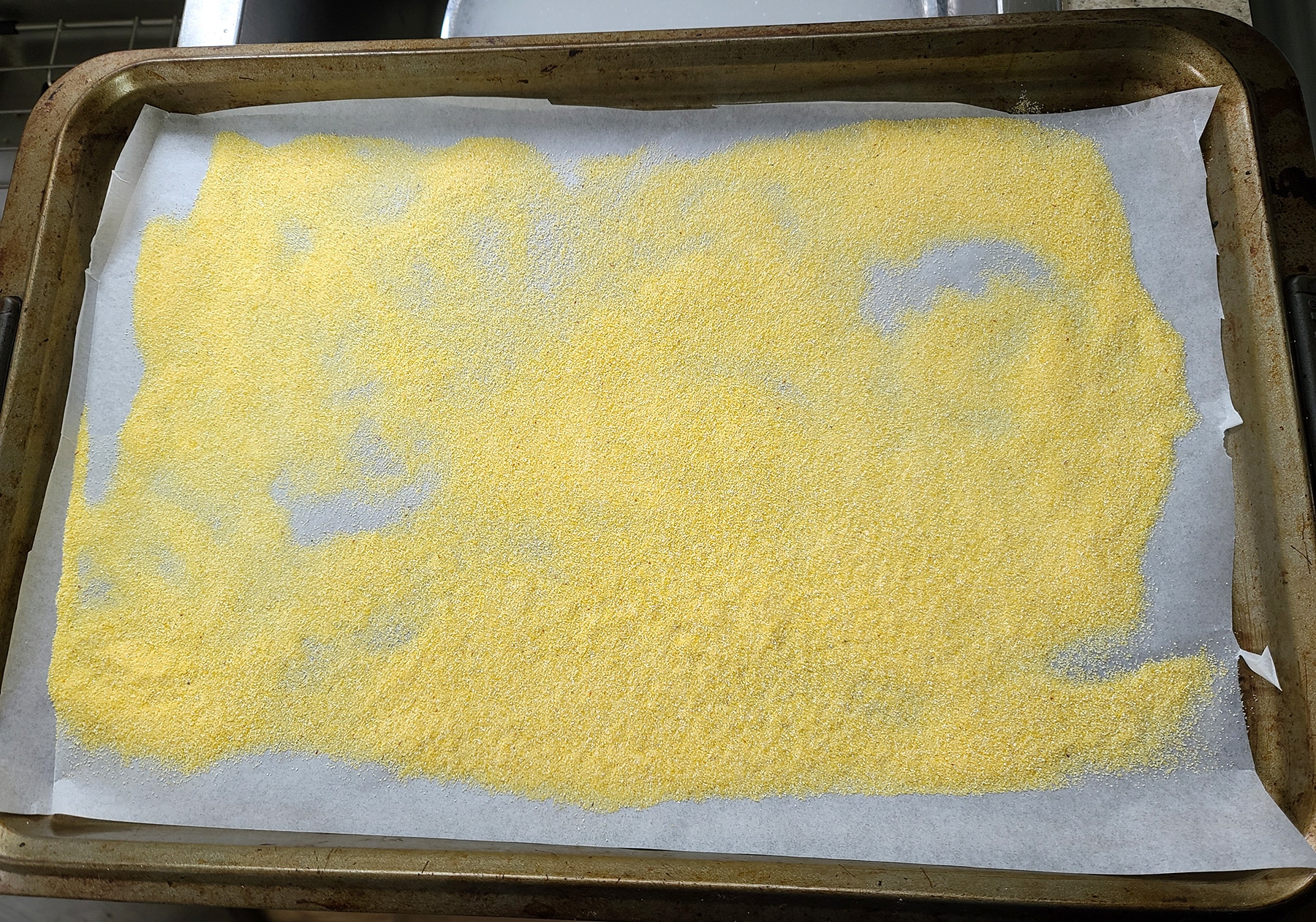 A baking sheet, lined with parchment paper and scattered with cornmeal.