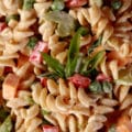 A close up view of a creamy rotini pasta salad made with rotini, red peppers, celery, peas, cheese, and green onions.
