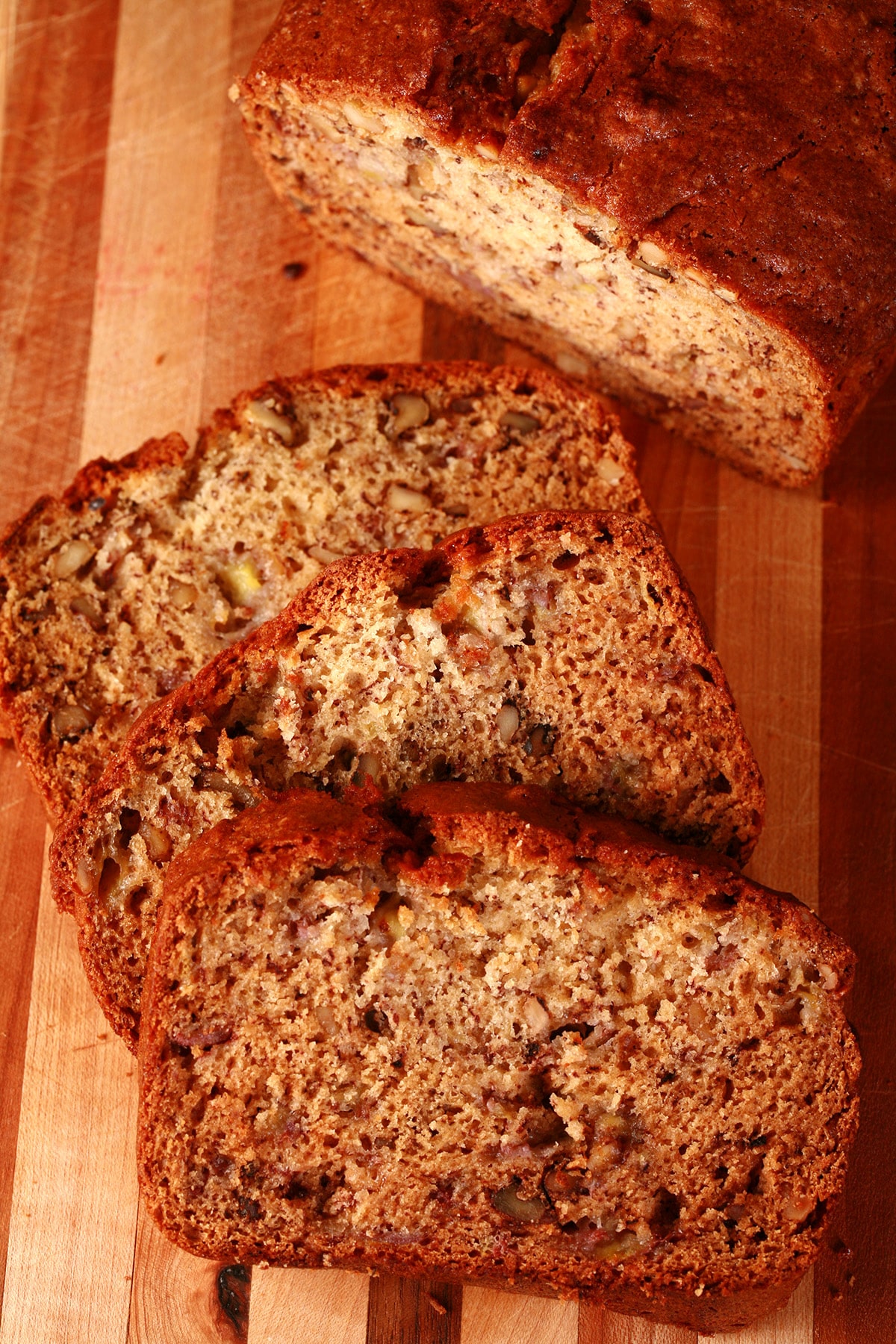 A sliced loaf of easy, moist banana bread with walnuts, on a wooden cutting board.
