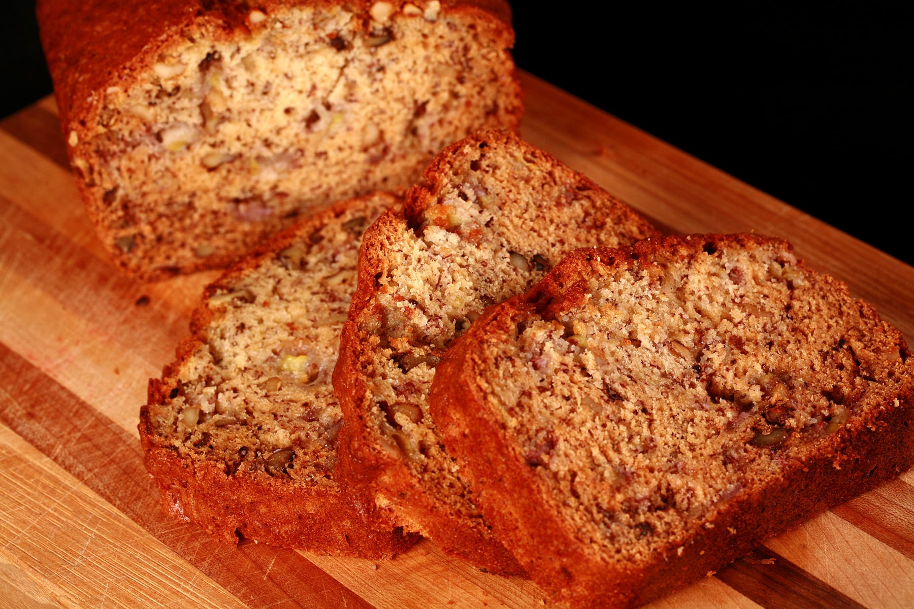 A sliced loaf of easy banana bread with walnuts, on a wooden cutting board.