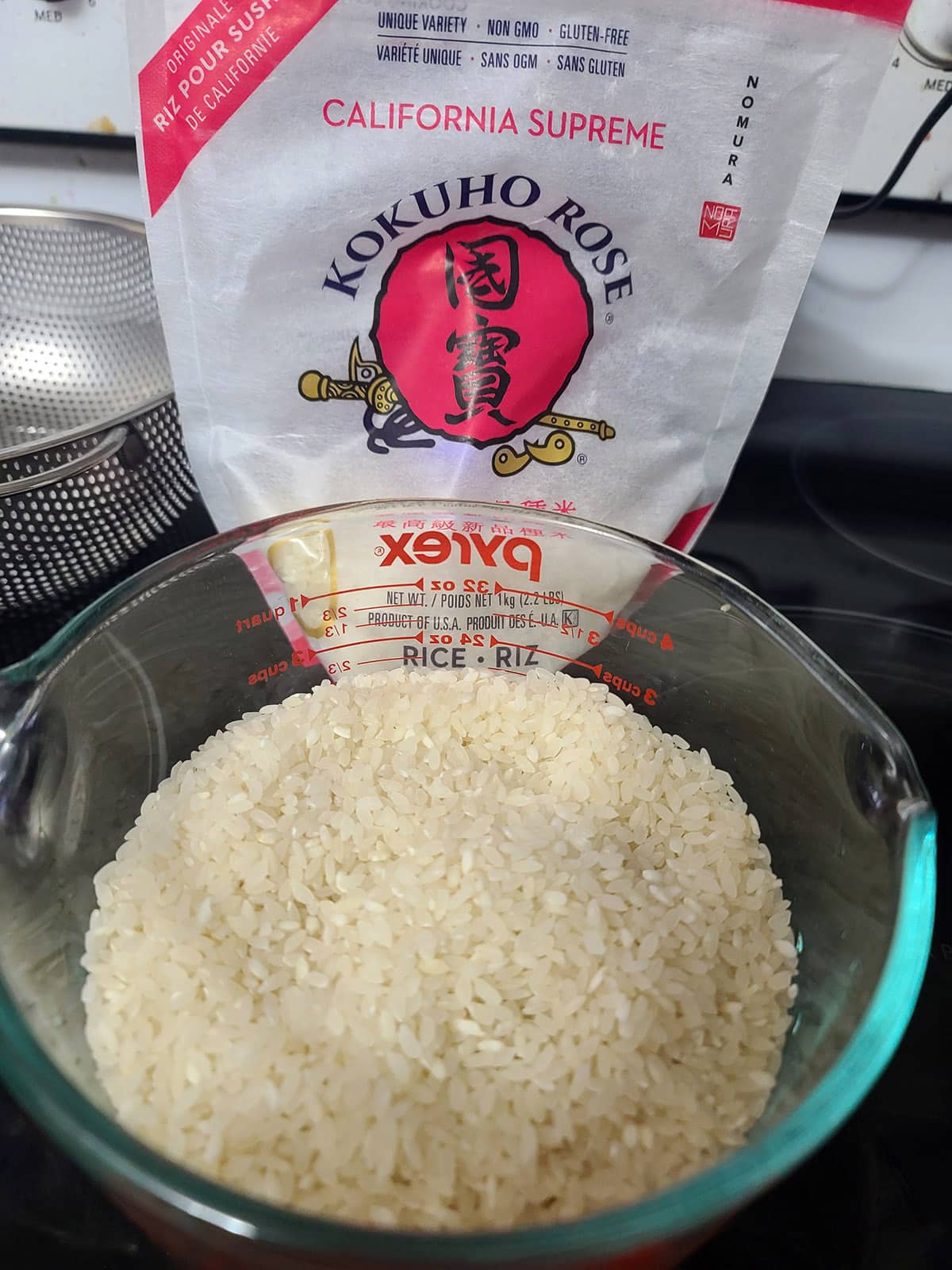 A large measuring cup of short grain rice in front of the bag of Kokuho rice it came out of.
