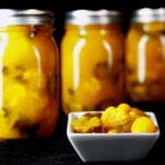 3 jars of bright yellow pickles, lined up behind a small bowl of mixed sweet mustard pickles.