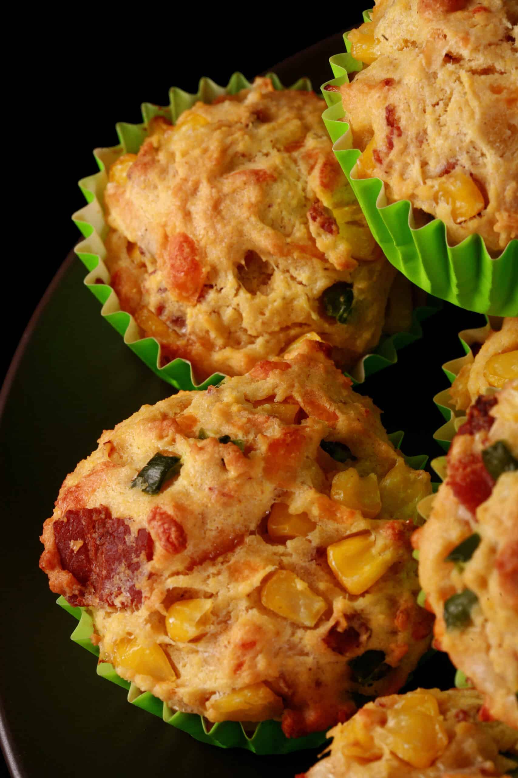 A plate of loaded breakfast corn muffins, with bacon, jalapeno, and corn kernels showing.