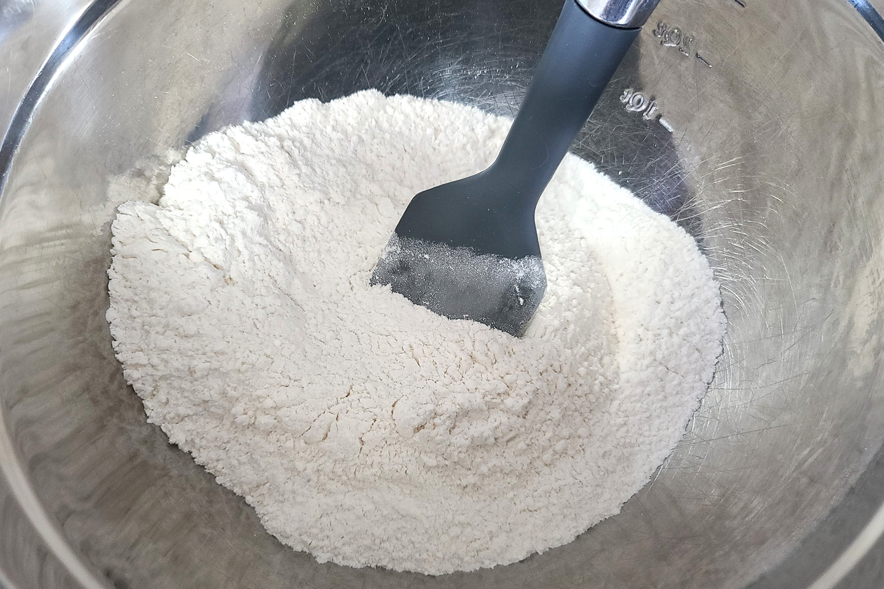 White coloured dry ingredients in a mixing bowl, with a silicone spatula.