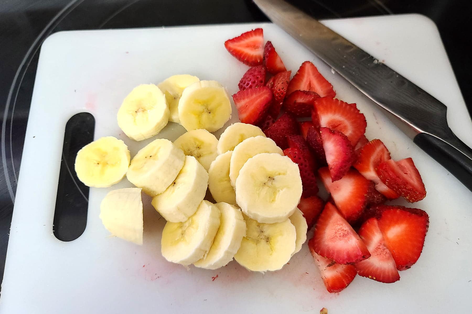 Sliced bananas and strawberries on a white cutting board.