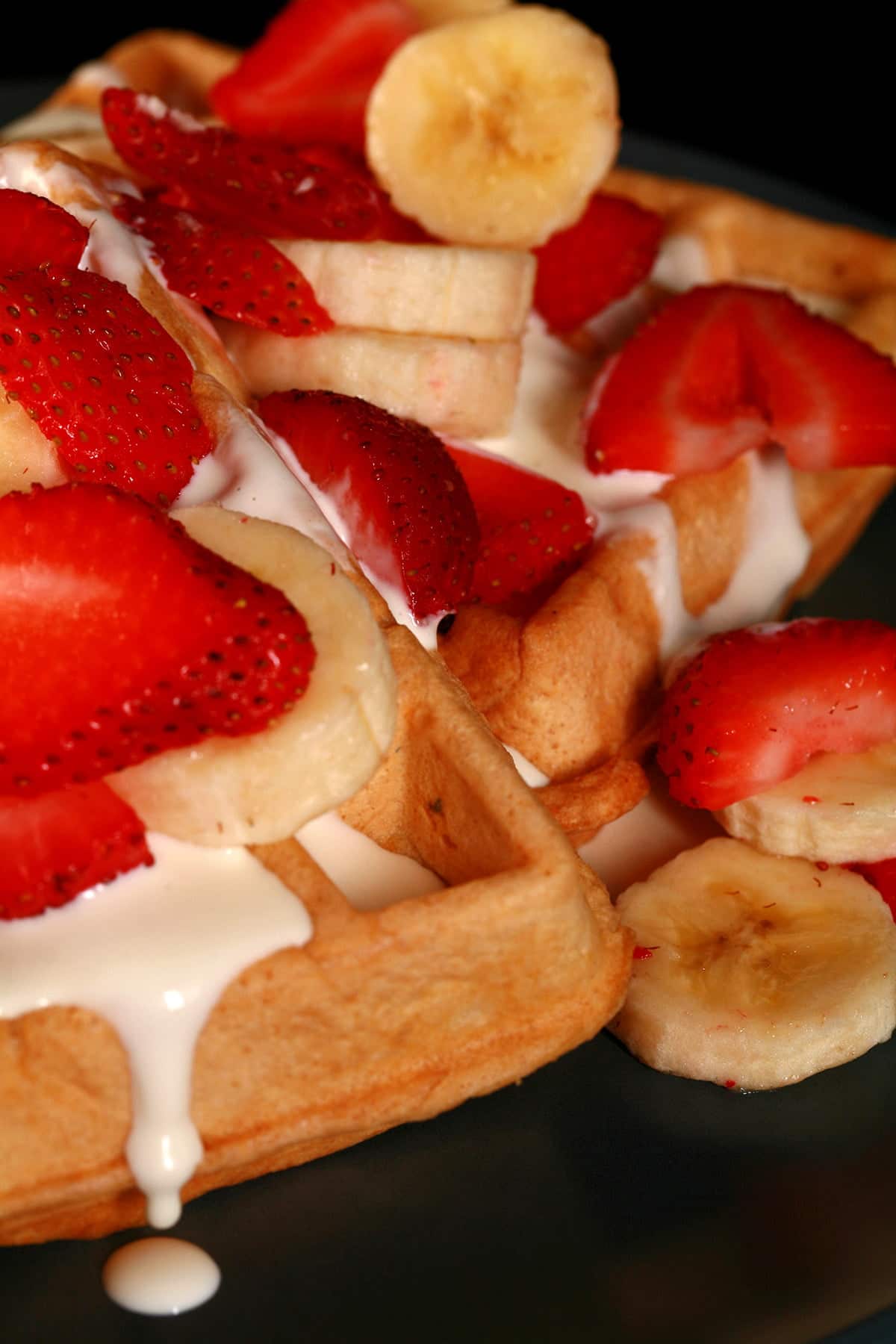 2 Ambrosia Belgian waffles - Belgian waffles with cream cheese sauce, topped with sliced strawberries and sliced bananas - on a blue plate.