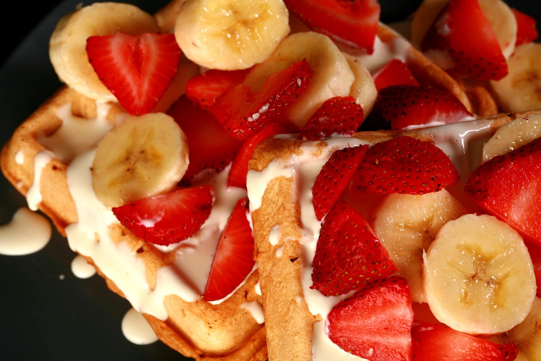 2 Ambrosia Waffles - Belgian waffles with cream cheese sauce, topped with sliced strawberries and sliced bananas - on a blue plate.