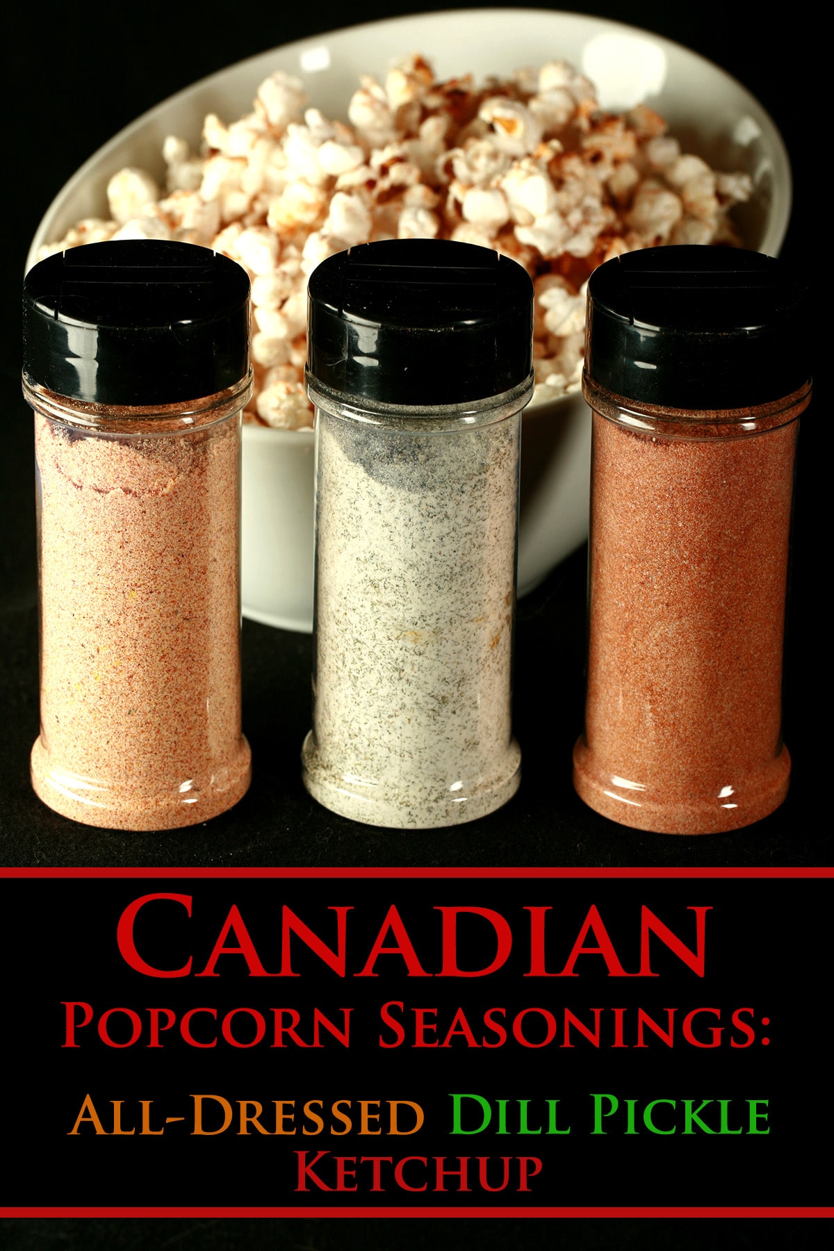 3 small canisters of popcorn seasoning - All Dressed, Dill Pickle, and Ketchup - are lined up in front of a large white bowl of seasoned popcorn.