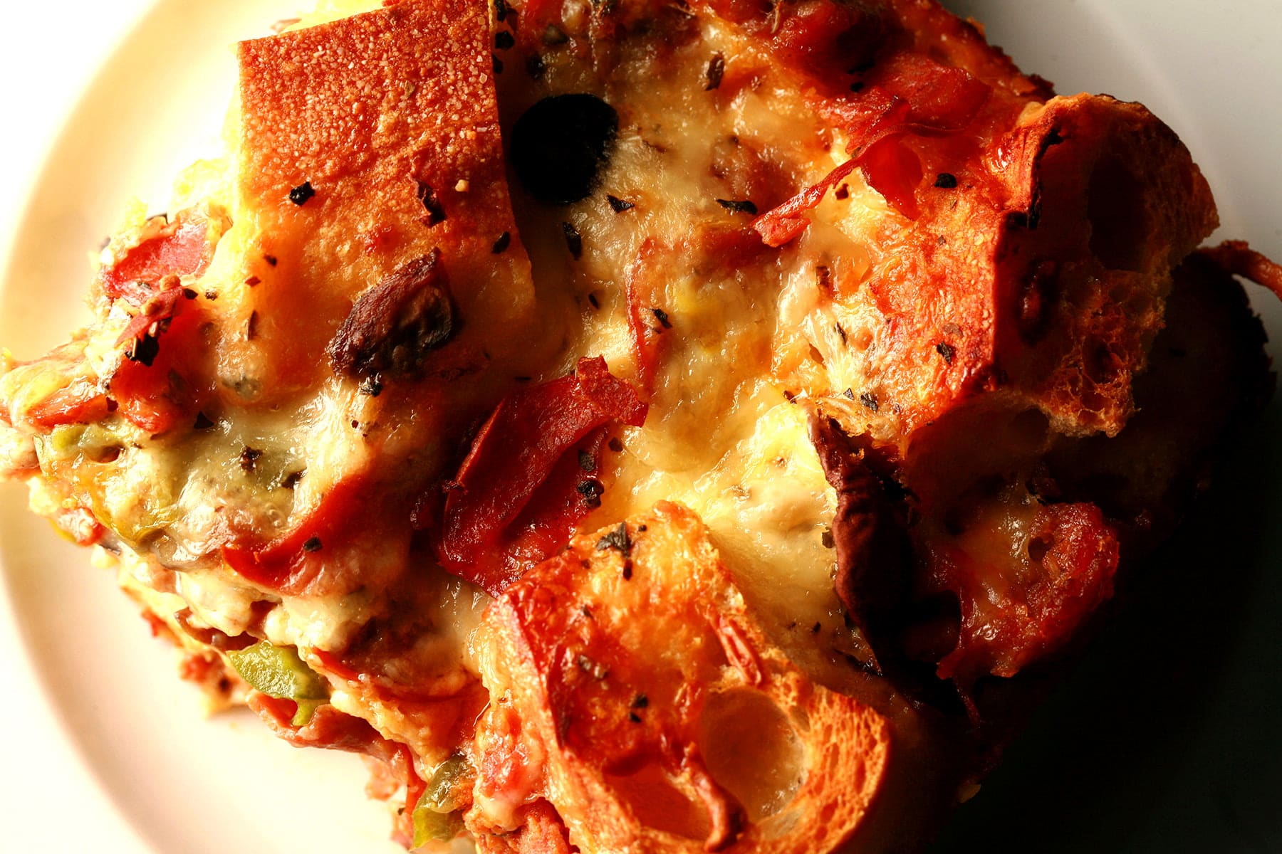 A square of deluxe pizza bread pudding: A brunch casserole featuring pepperoni, sausage, mushrooms, green peppers, black olives, marinara sauce, and cheese.