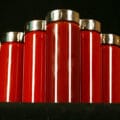 Seven tall, slender glass bottles filled with varying shades of dark red BBQ sauce - Replica Diana Sauce. The jars all have matching stainless lids, and are arranged in a V formation.