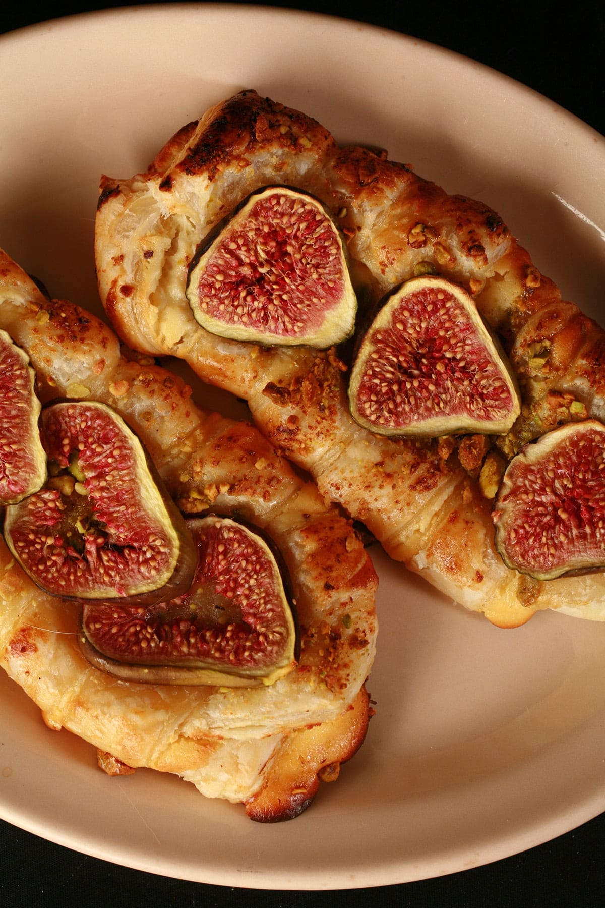 A close up view of two fig, honey, and goat cheese strudel pastries on a tan coloured plate.