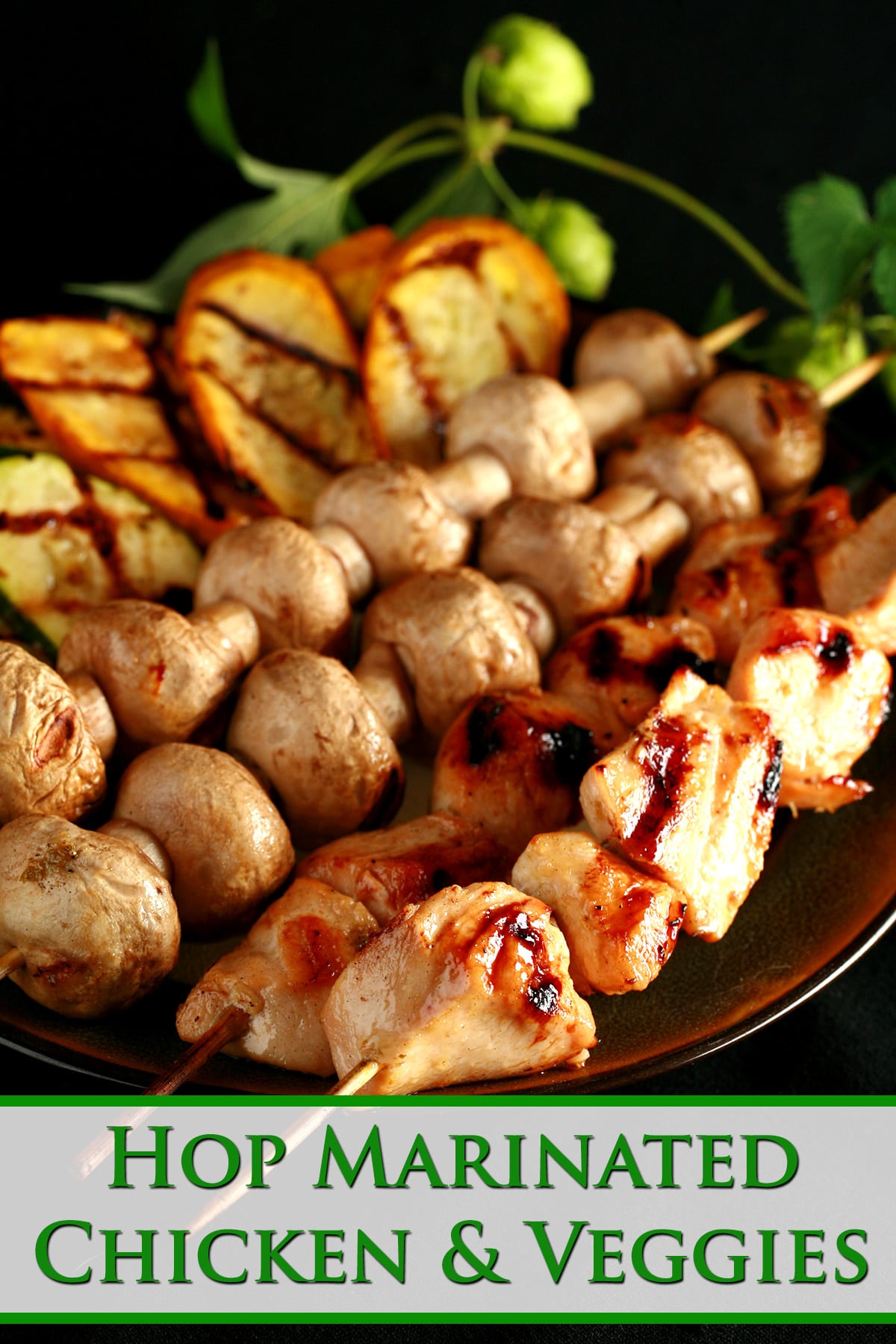 Skewers of hop-marinated grilled chicken, mushrooms, and zucchini are lined up on a brown platter. A hop bine with flowers wraps around the back end of the platter.