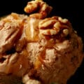 A glass dessert flute has several scoops of homemade maple walnut ice cream stacked in it. It has been drizzled with maple syrup and topped with toasted walnuts.