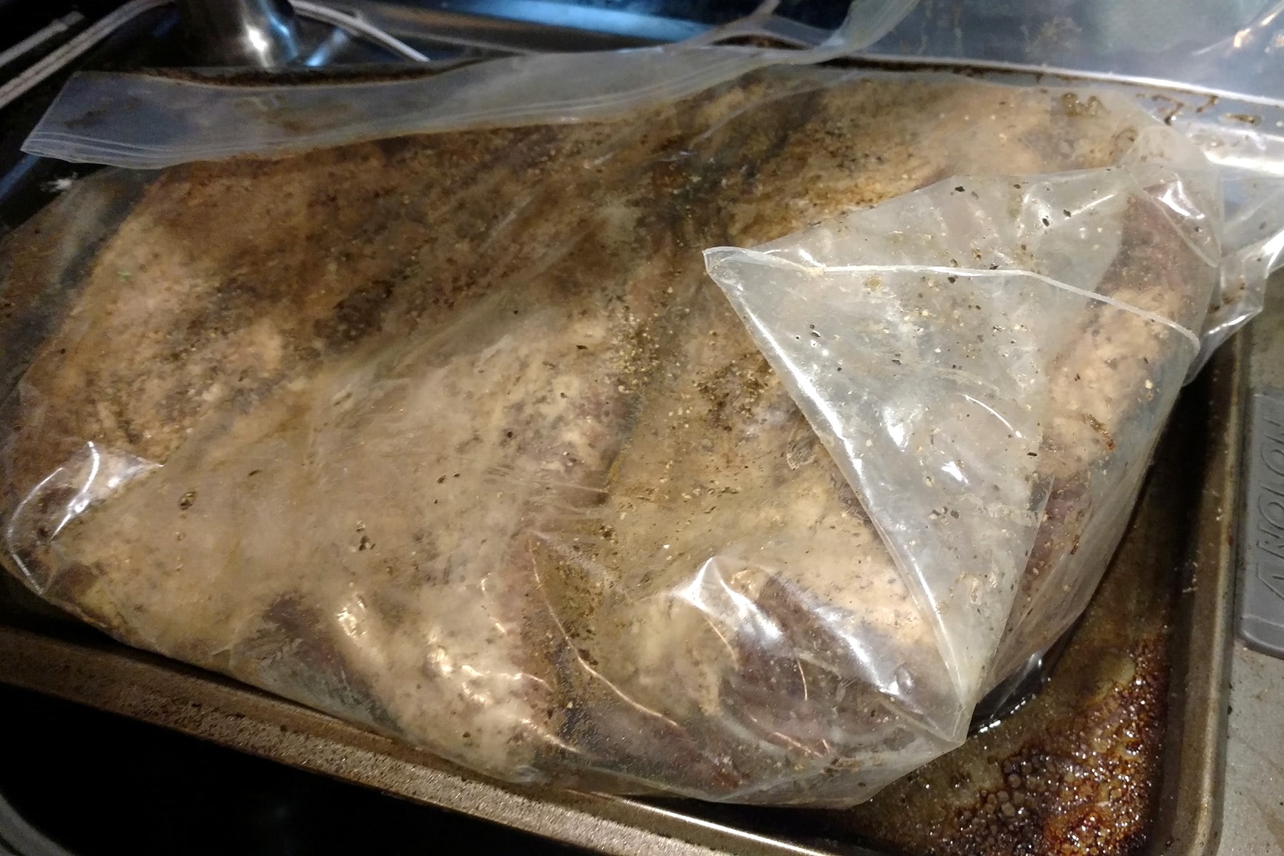 A large slab of meat is curing in a large plastic bag.