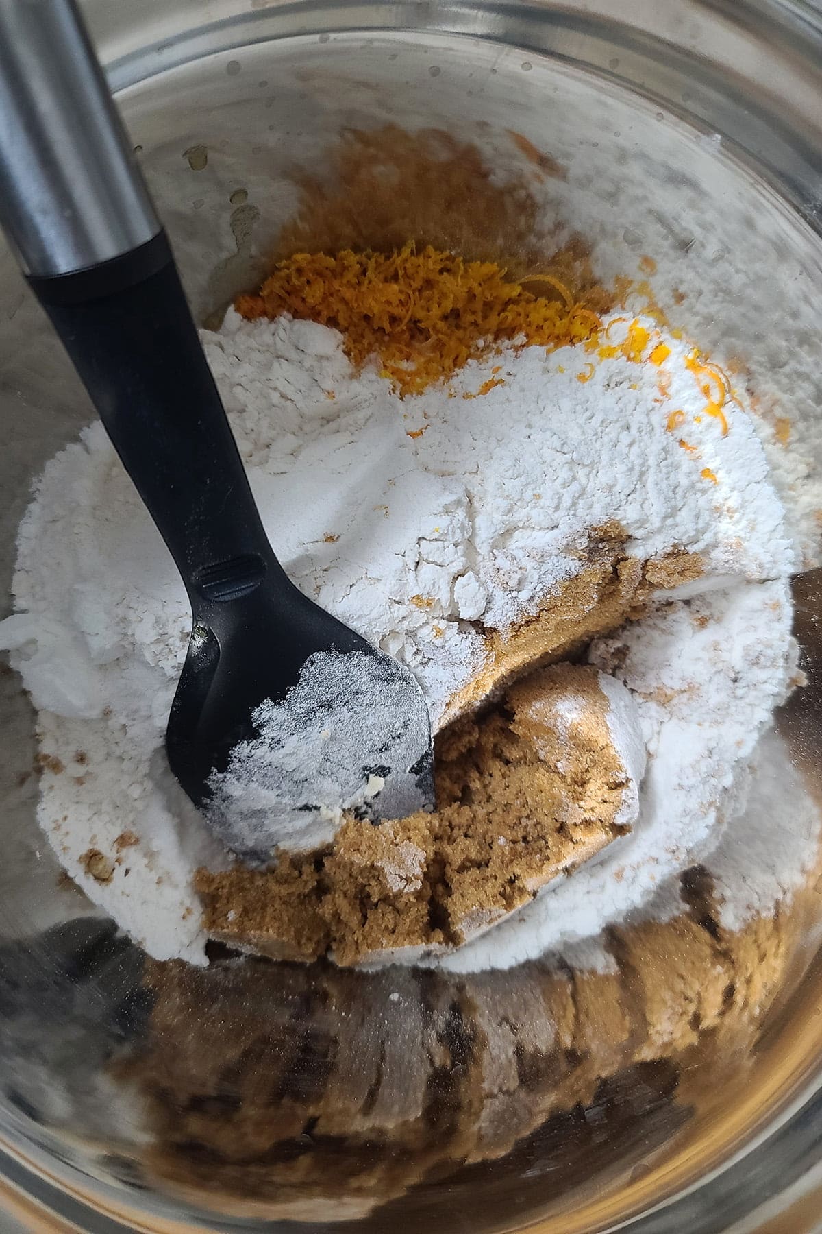 FLour, orange zest, and brown sugar are seen being stirred together in a large bowl.