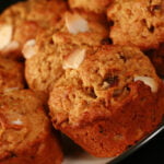 A plate of orange date and almond muffins. They are an orangey brown colour, with slices of almonds and chunks of dates visible throughout.