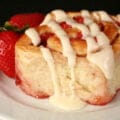 A strawberry orange roll on a white plate, with 2 fresh strawberries next to it.