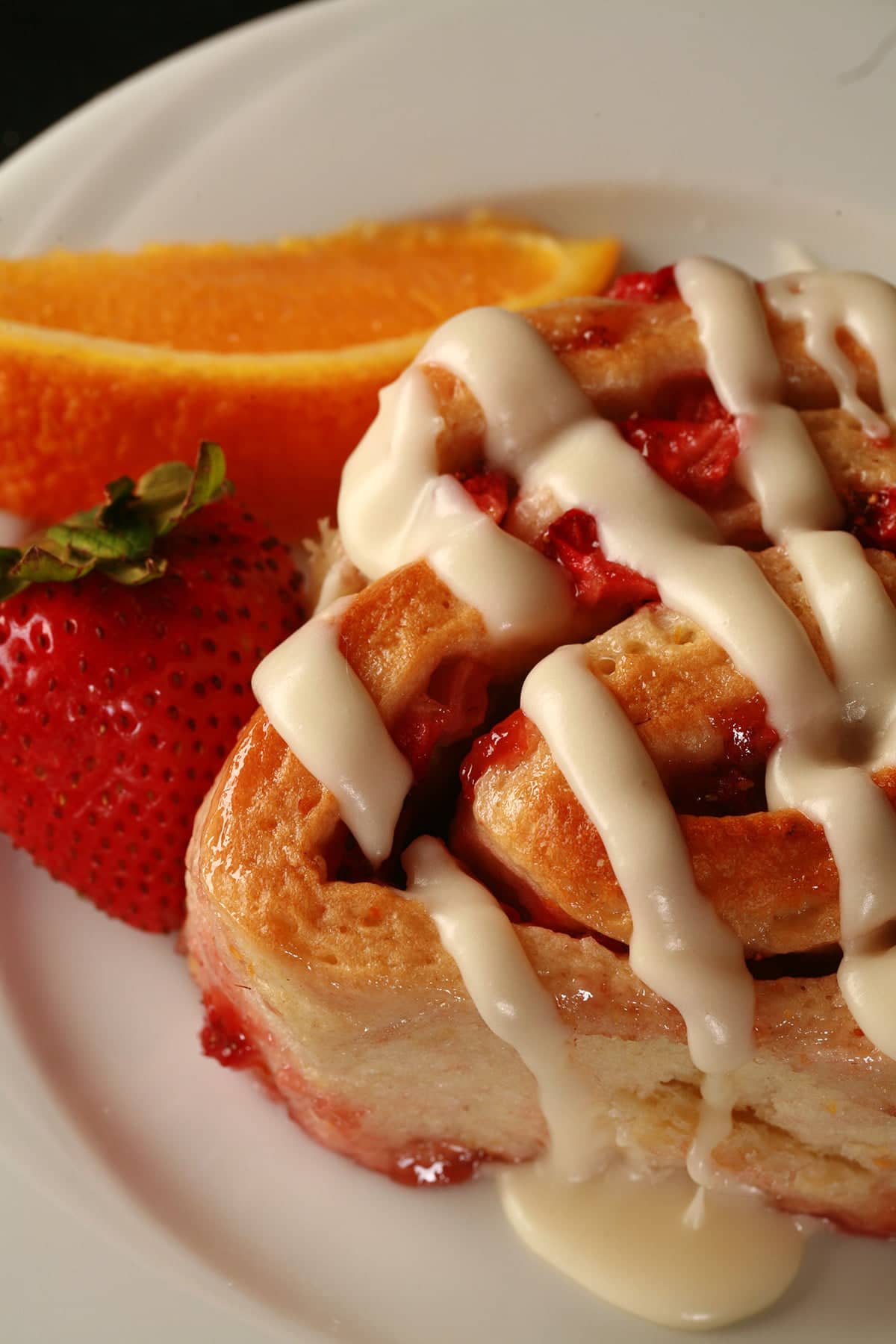 An orange strawberry roll on a white plate, with a fresh strawberry and an orange slice next to it