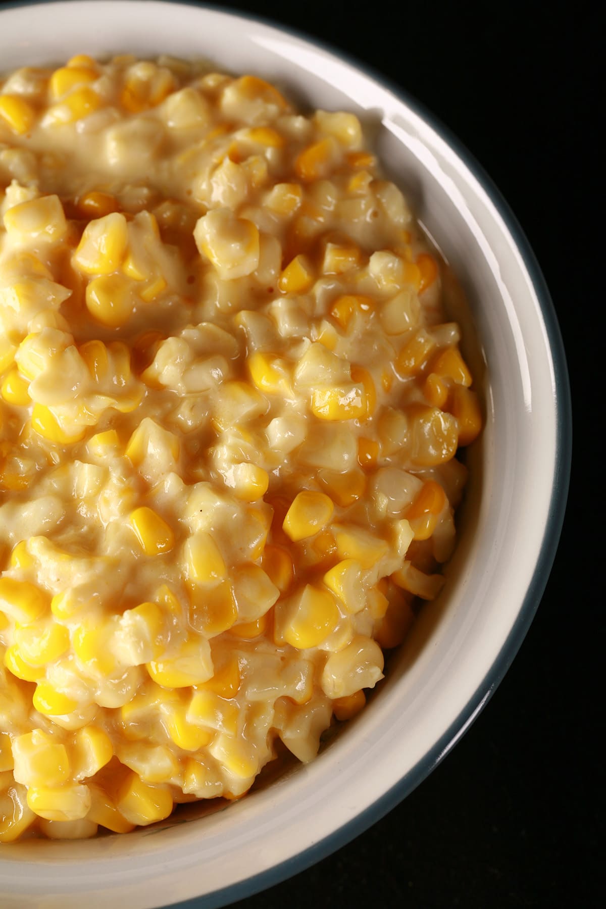 A large white bowl full of homemade creamed corn, against a black background.