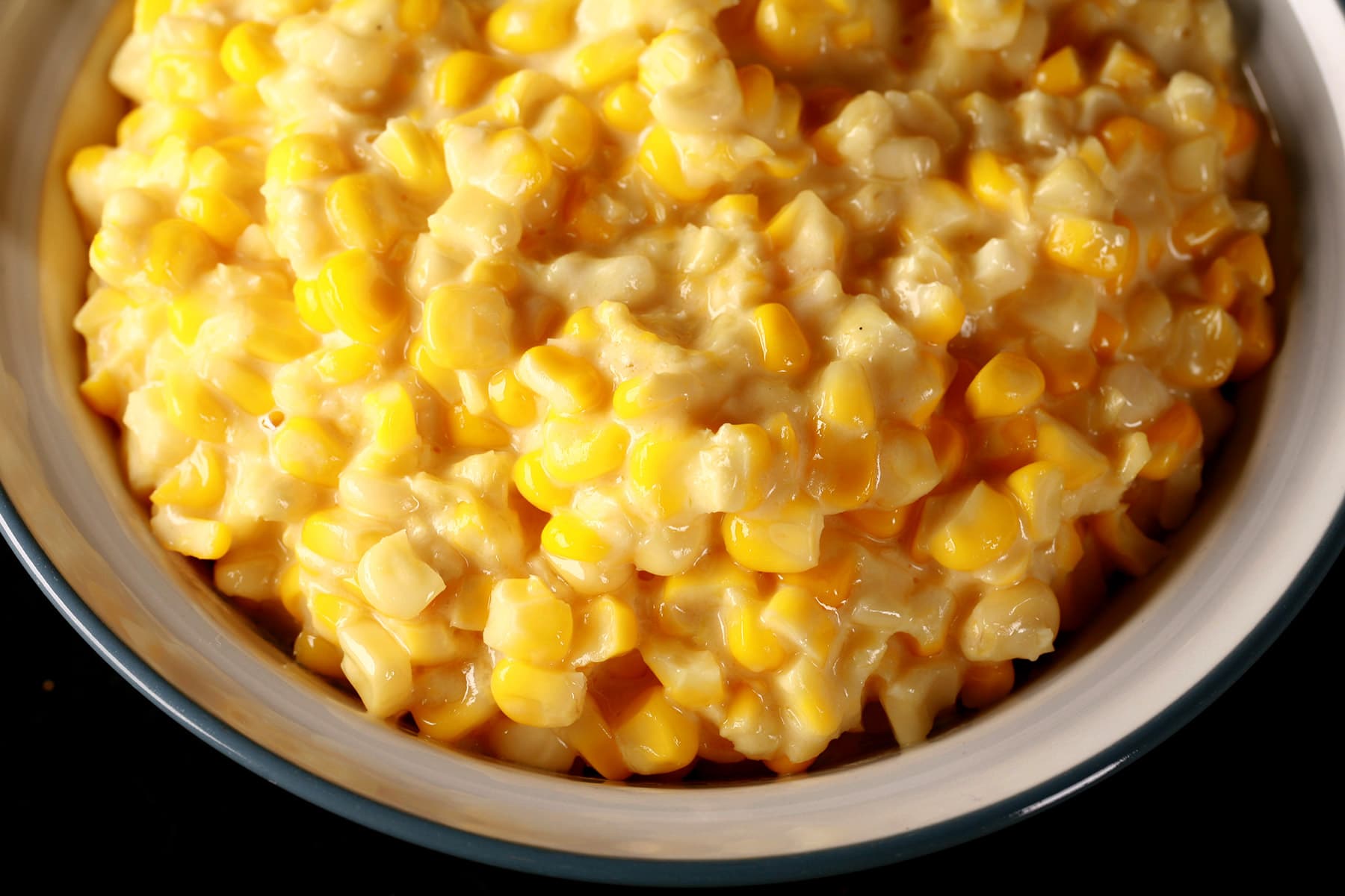 A large white bowl full of homemade creamed corn, against a black background.