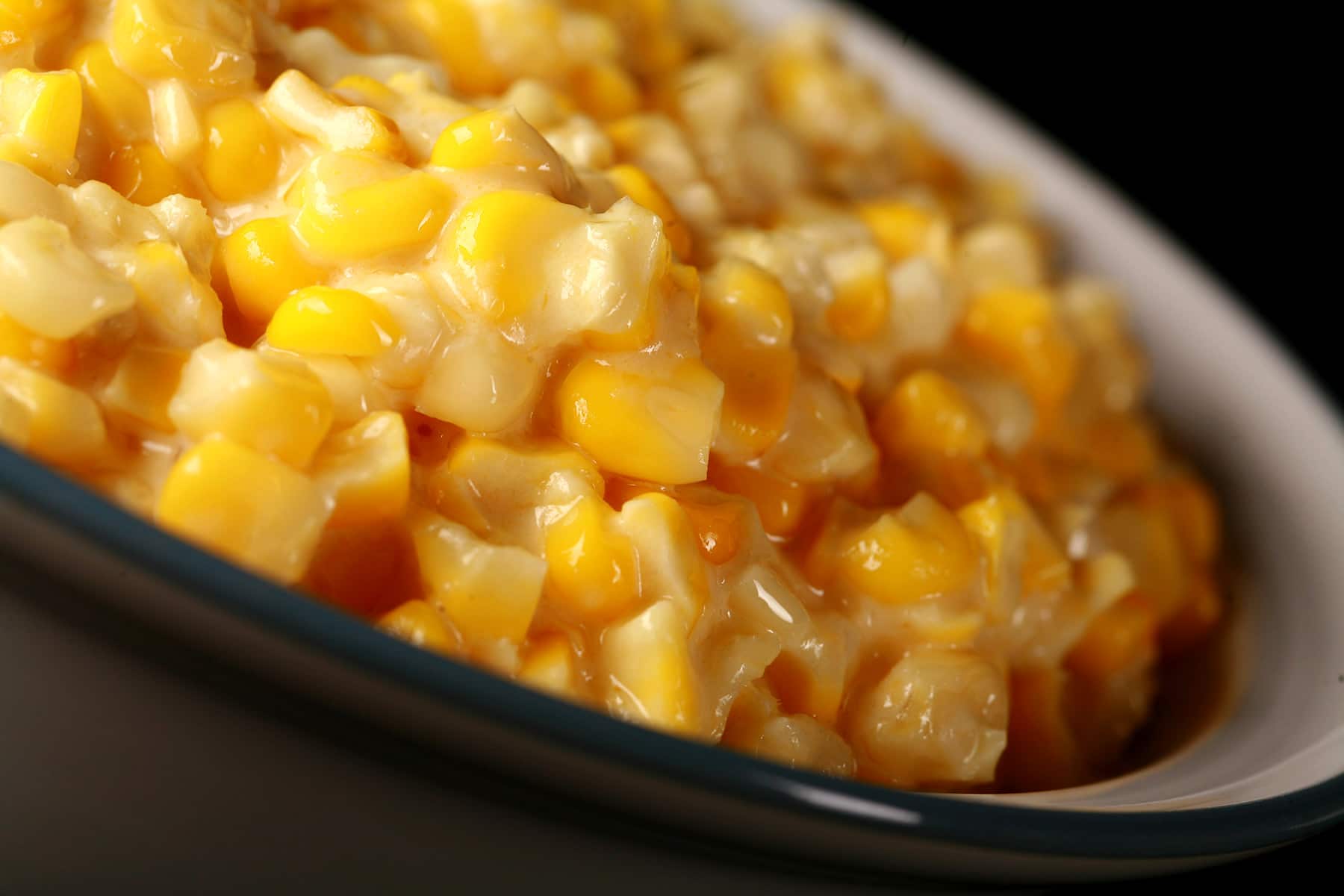 A large white bowl full of homemade creamed corn, against a black background.