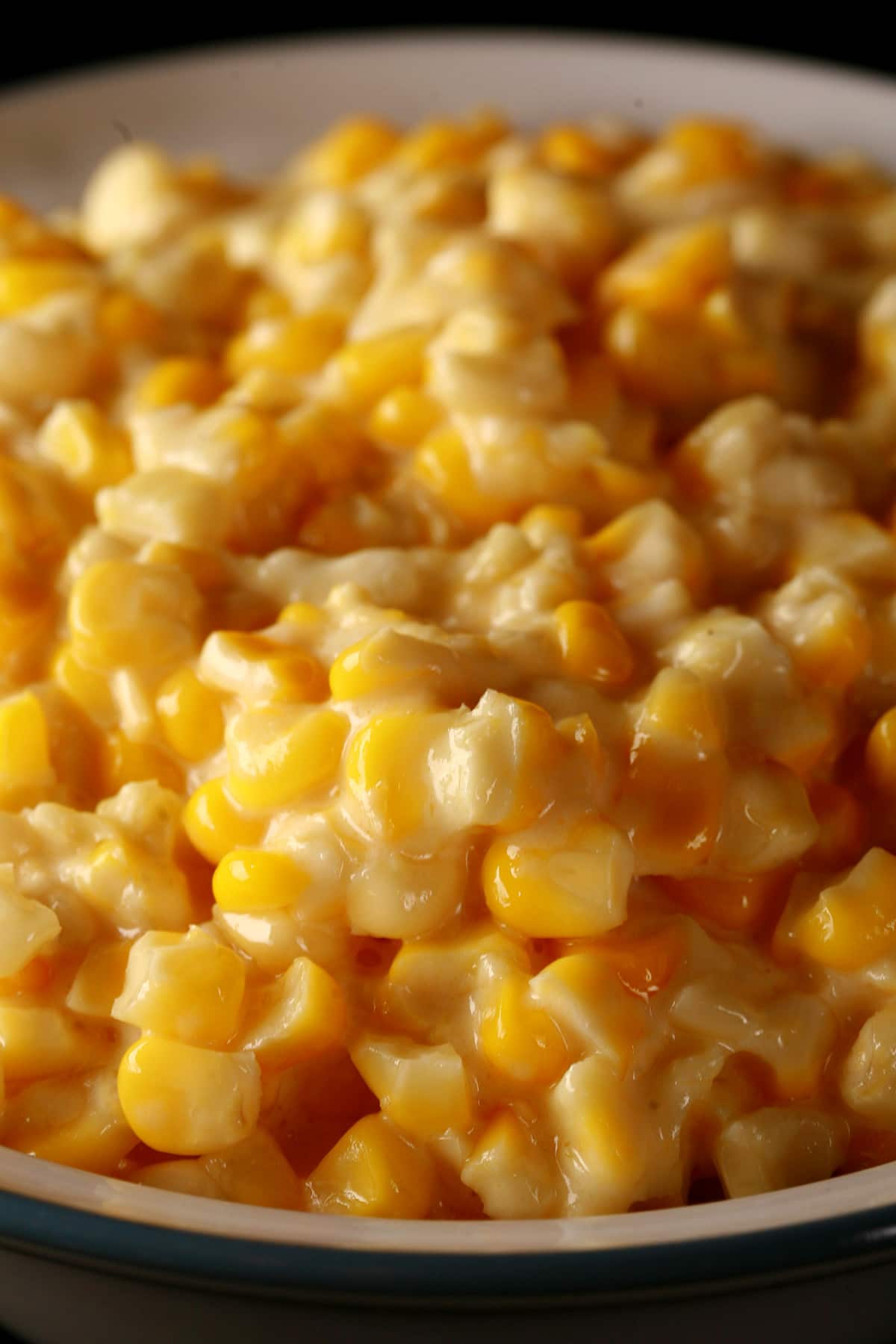 A large white bowl full of homemade creamed corn, against a black background.A large white bowl full of homemade creamed corn, against a black background.