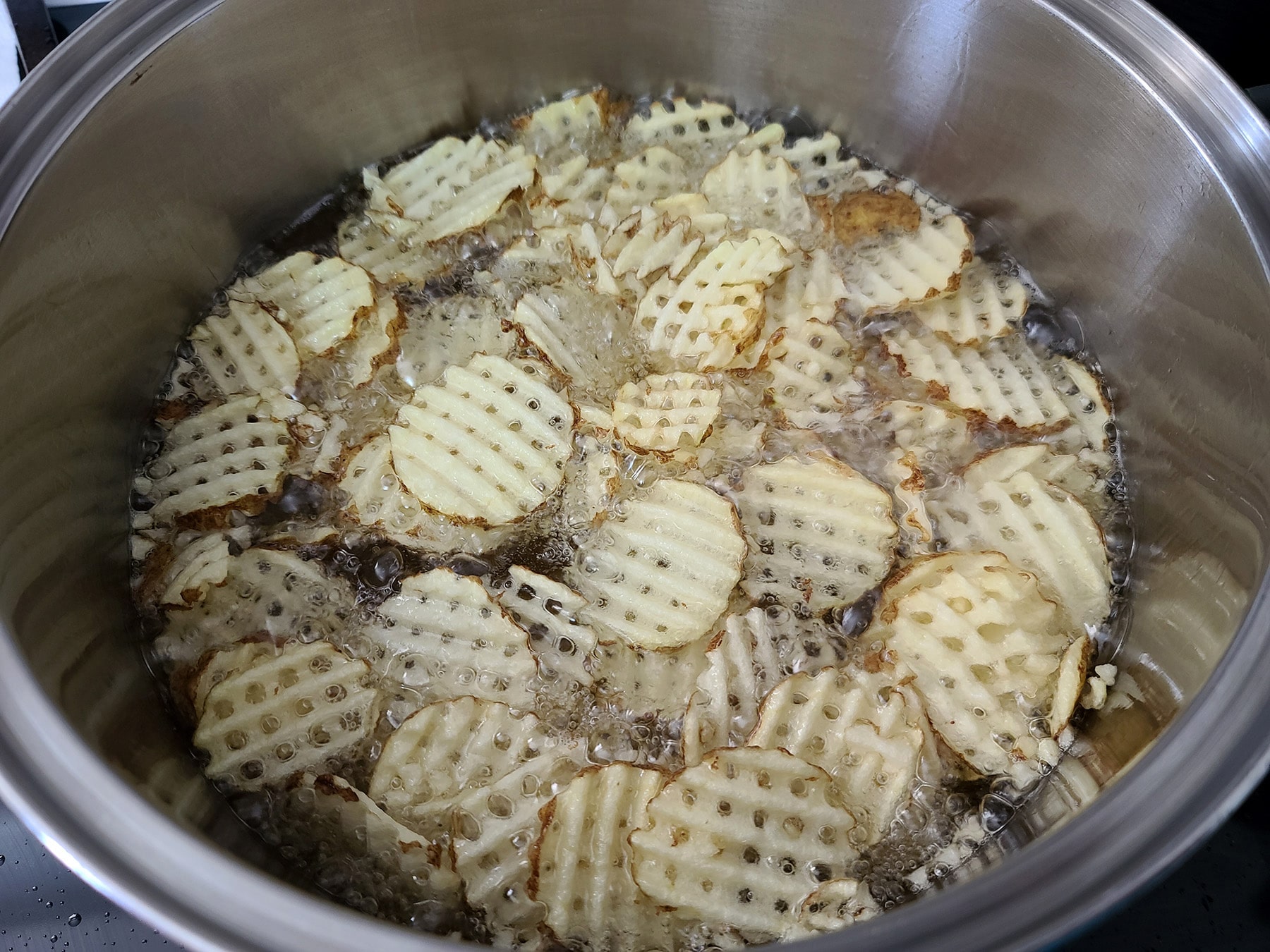 A large metal pot of oil, deep frying waffle cut potatoes. They are pale and white at this point.