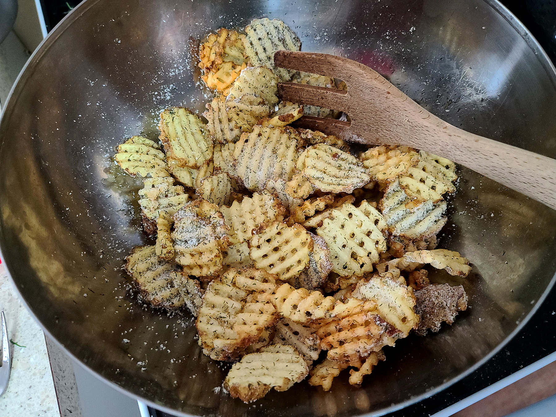Waffle cut fries in a metal bowl, being tossed with dill pickle seasoning.