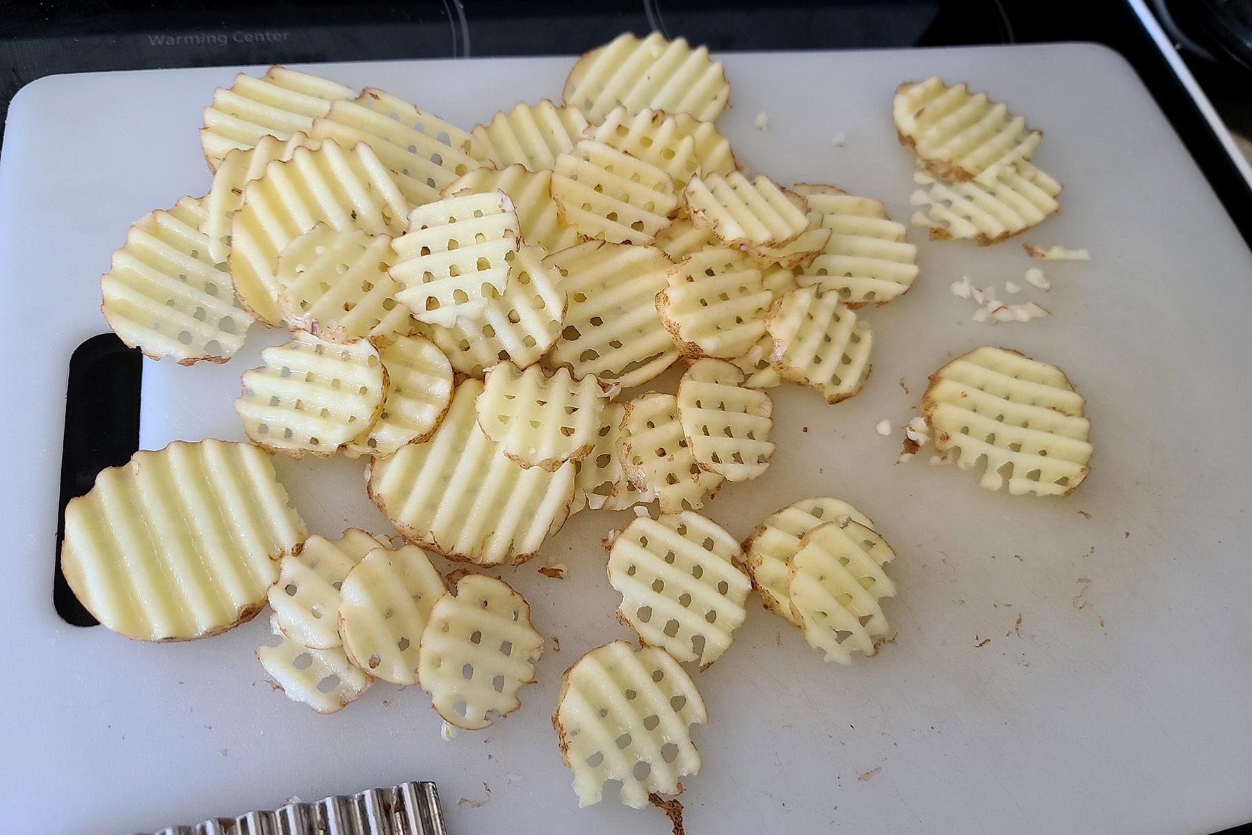 A pile of waffle cut potatoes on a cutting board.