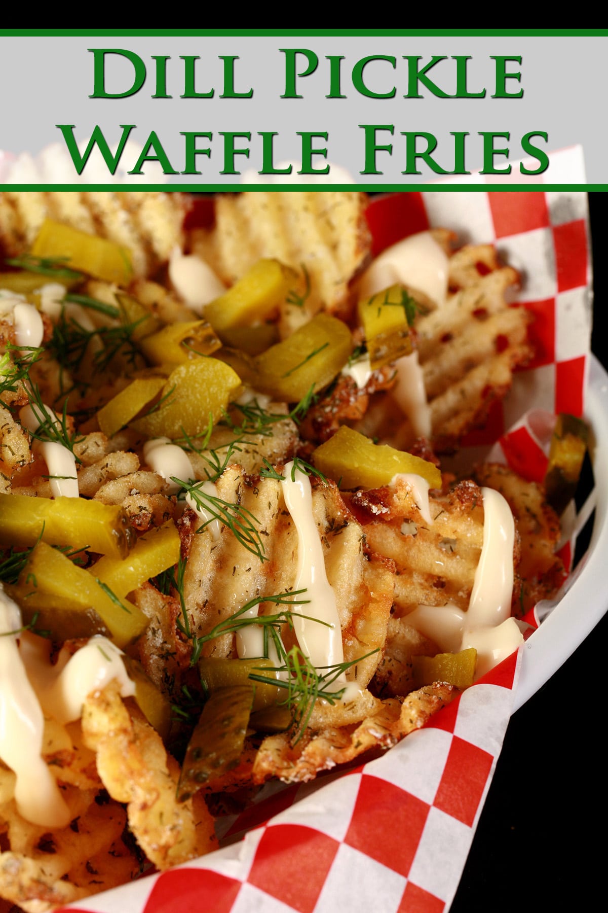 Waffle cut fries, in a white basket lined with red and white checkered paper. The fries are drizzled with roasted garlic aioi and topped with chopped dill and chopped pickles. Green Text overlay says Dill Pickle Waffle Fries.
