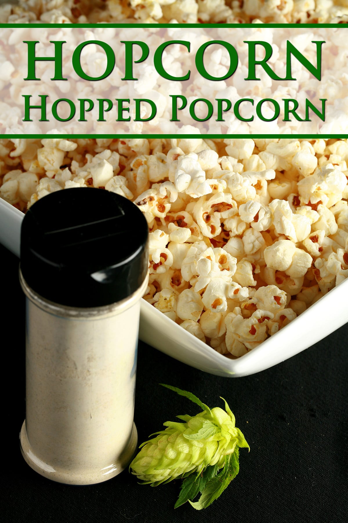A large rectangular bowl holds hop-seasoned popcorn - hopcorn! There is a small canister of the popcorn seasoning, and a fresh hop flower next to the bowl.