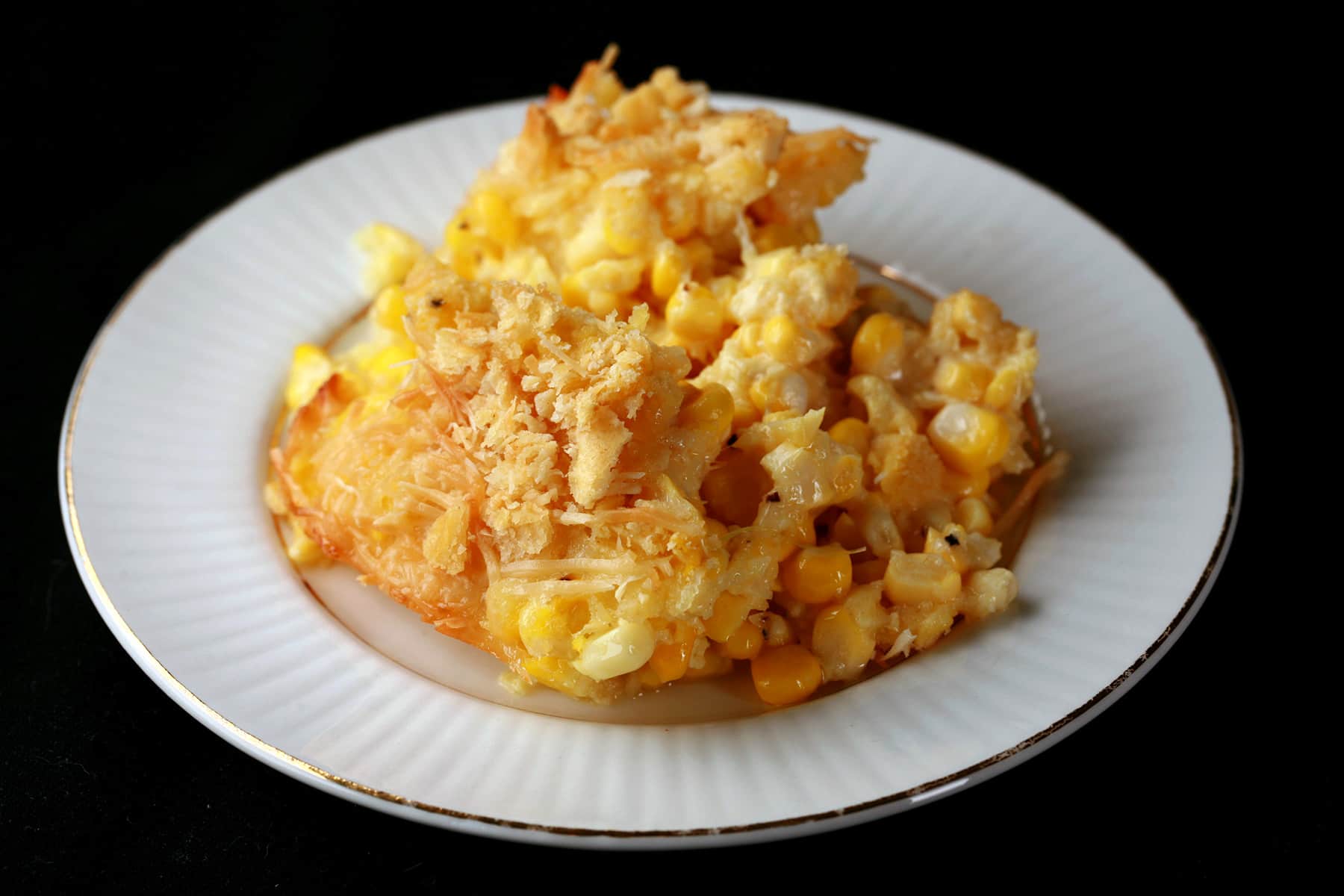A serving of scalloped corn - fresh sweet corn, cheese, crackers, and more - on a small white plate.