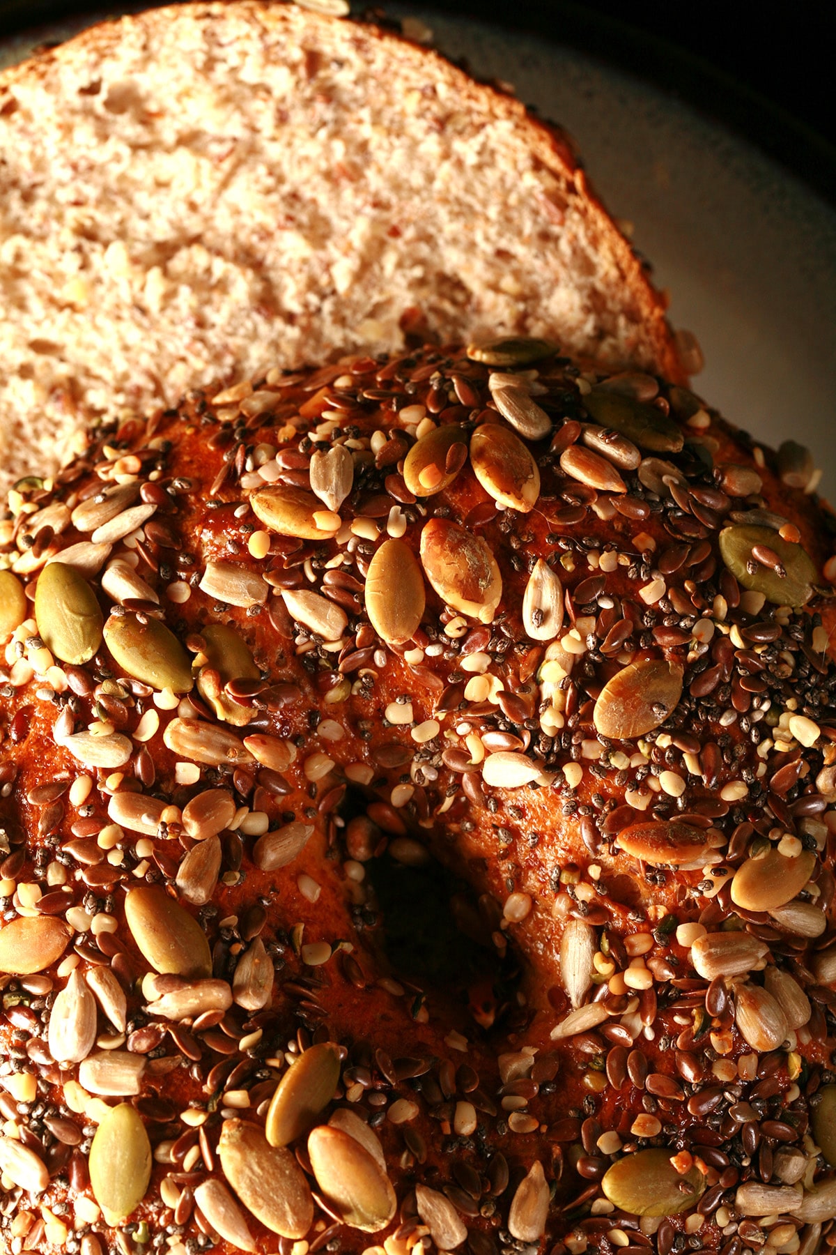 A whole wheat and flax bagel, sliced and served on a small plate. The top side of the bagel is covered in a mix of seeds - pumpkin, sunflower, sesame, chia, and poppy.