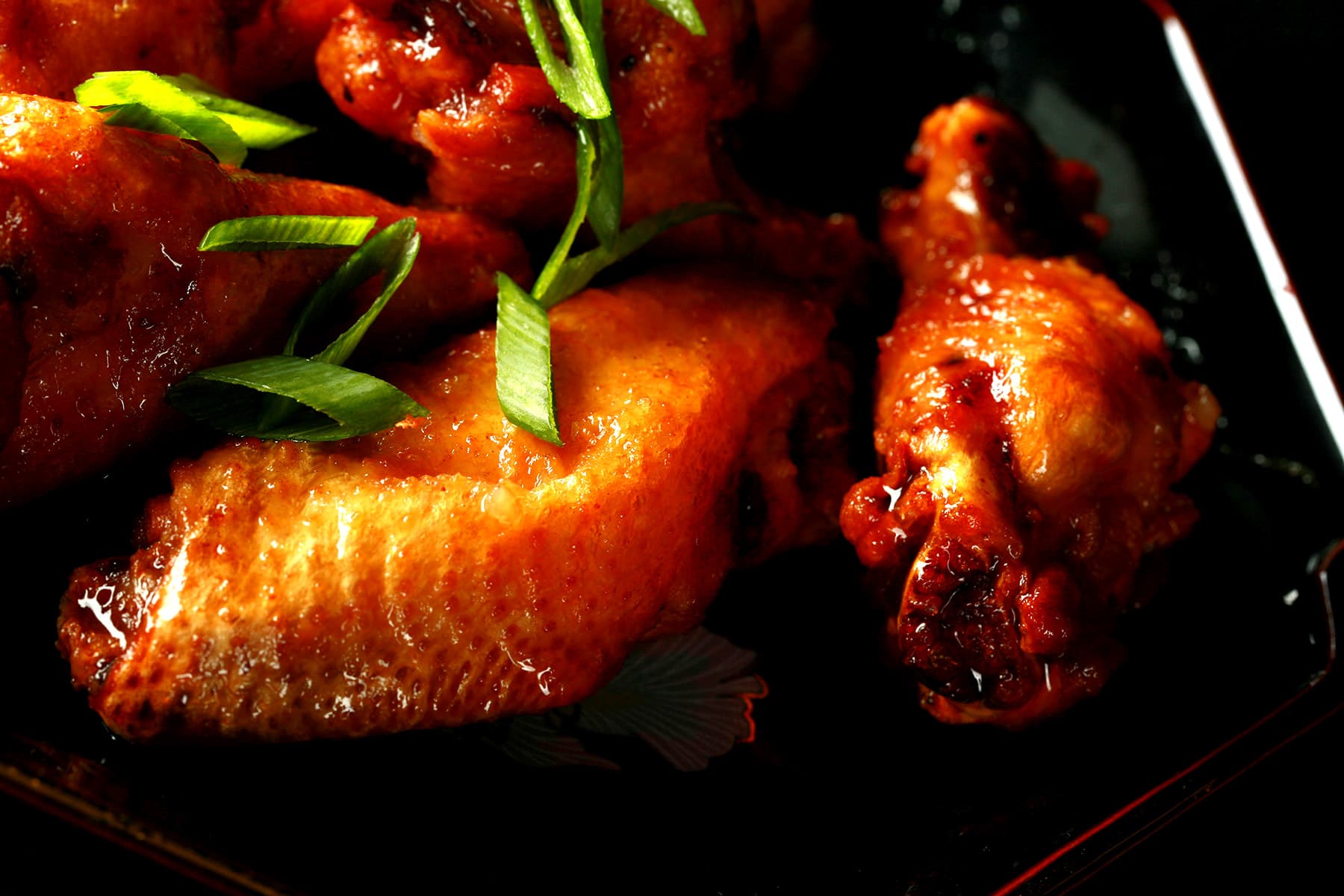 A small black plate with a pile of Spicy Ginger Wings piled on it, topped with slices of green onion.
